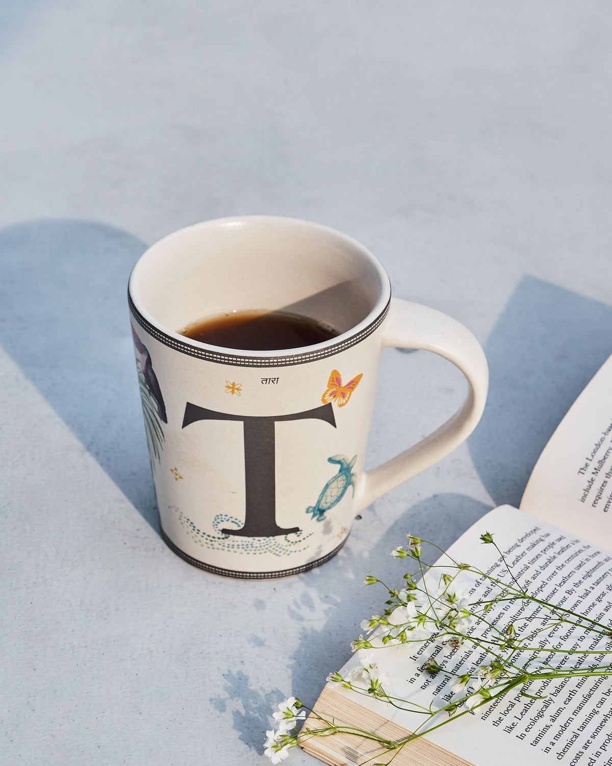 Tara mug with a large black letter T and butterfly and turtle motifs.