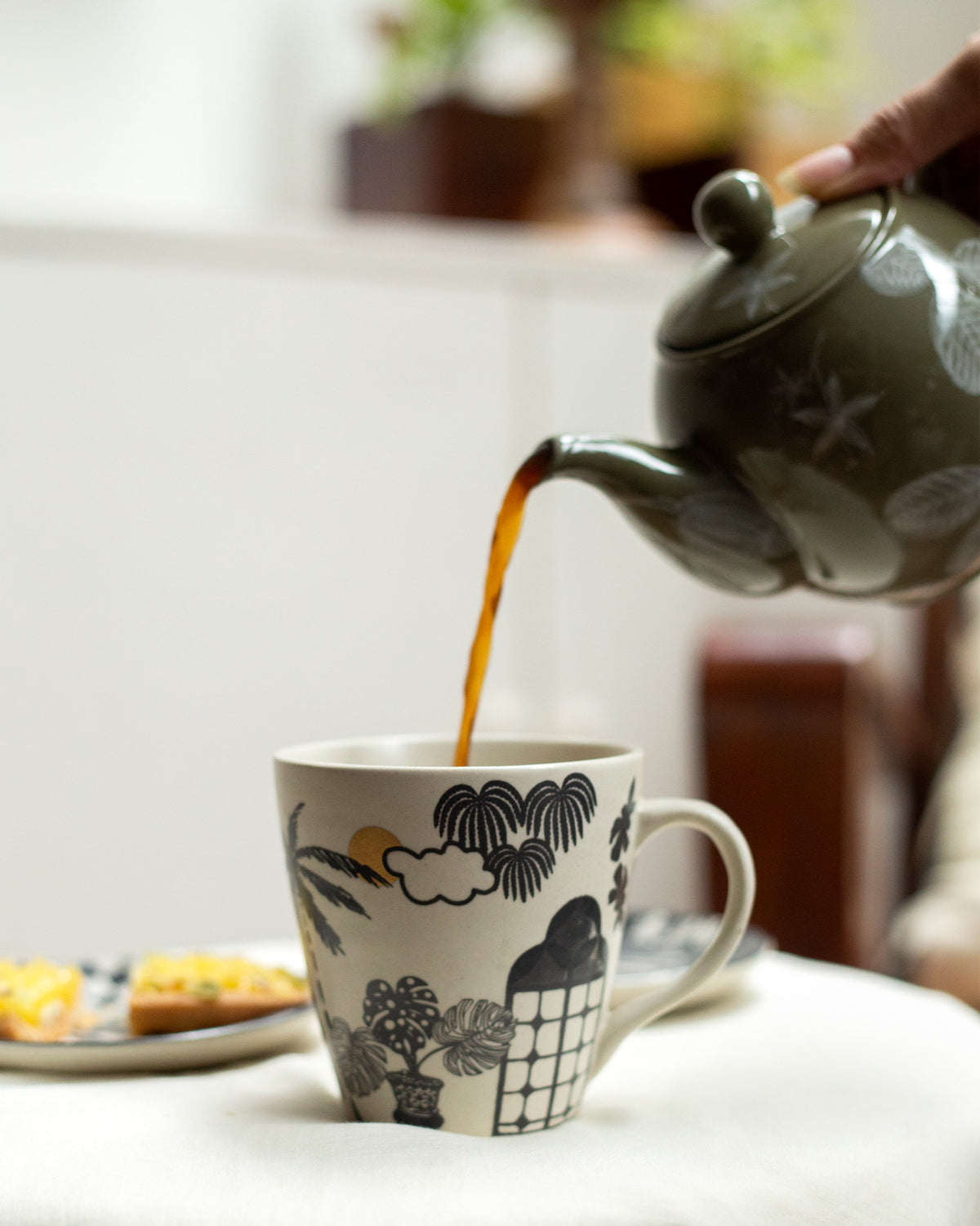 Tea being poured into a Mandovi Palm Mug with a palm and monstera print.