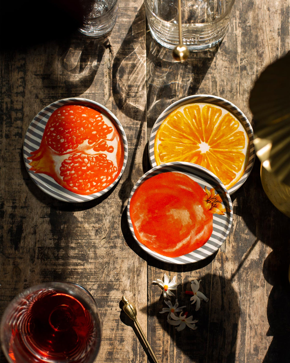 Nimbu & Anar coasters with pomegranate and citrus prints, shown with drinks.