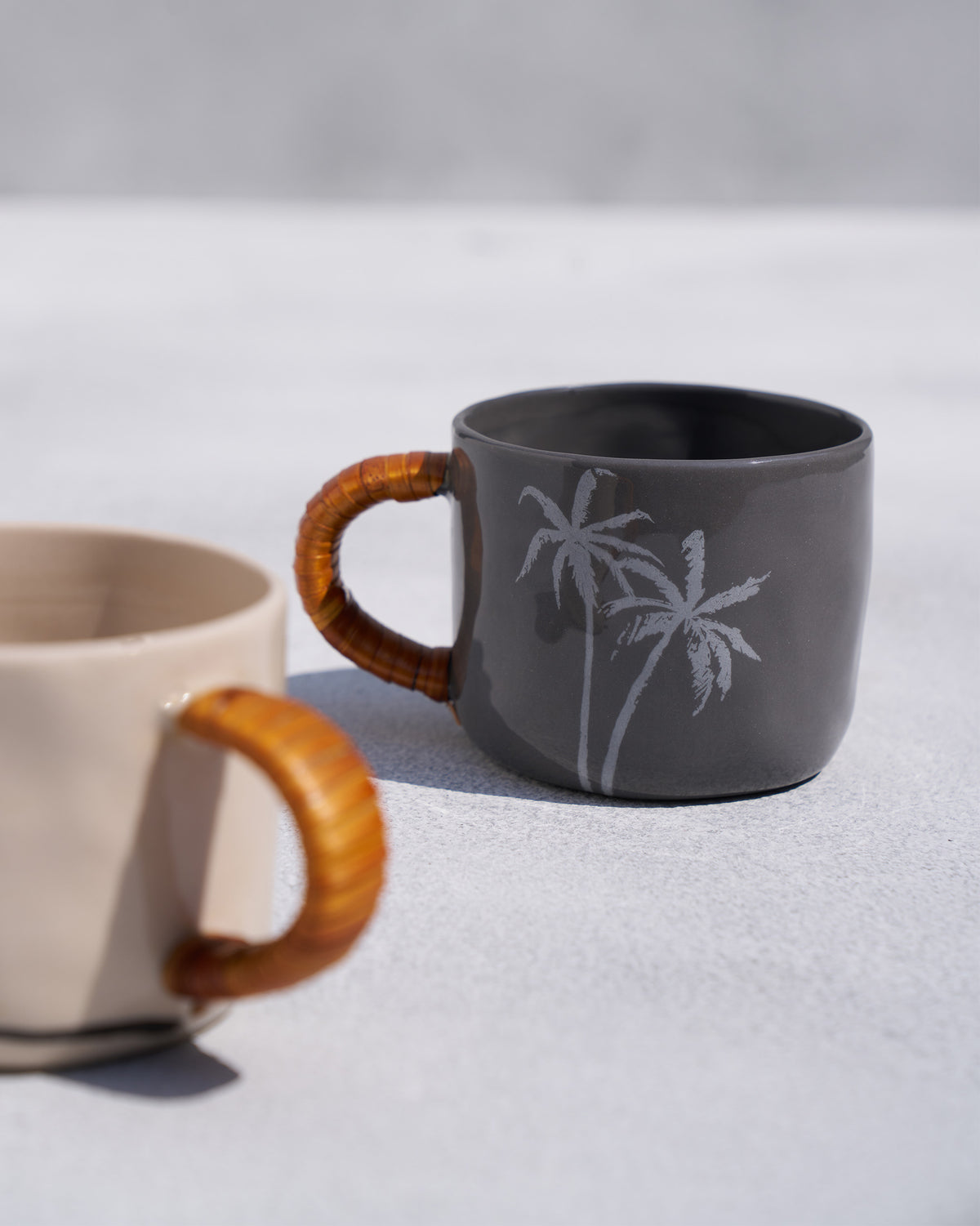 Close-up of a charcoal Mandovi mug with palm trees and a rattan handle.