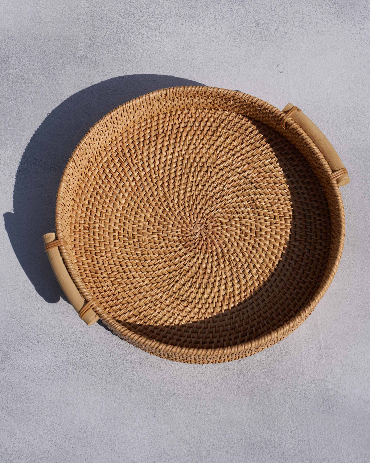 Overhead view of a round rattan tray showing spiral weave and wooden handles.