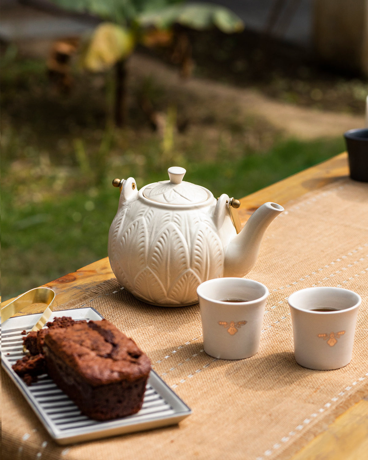 Teesta teapot with embossed leaves beside bee motif cups.