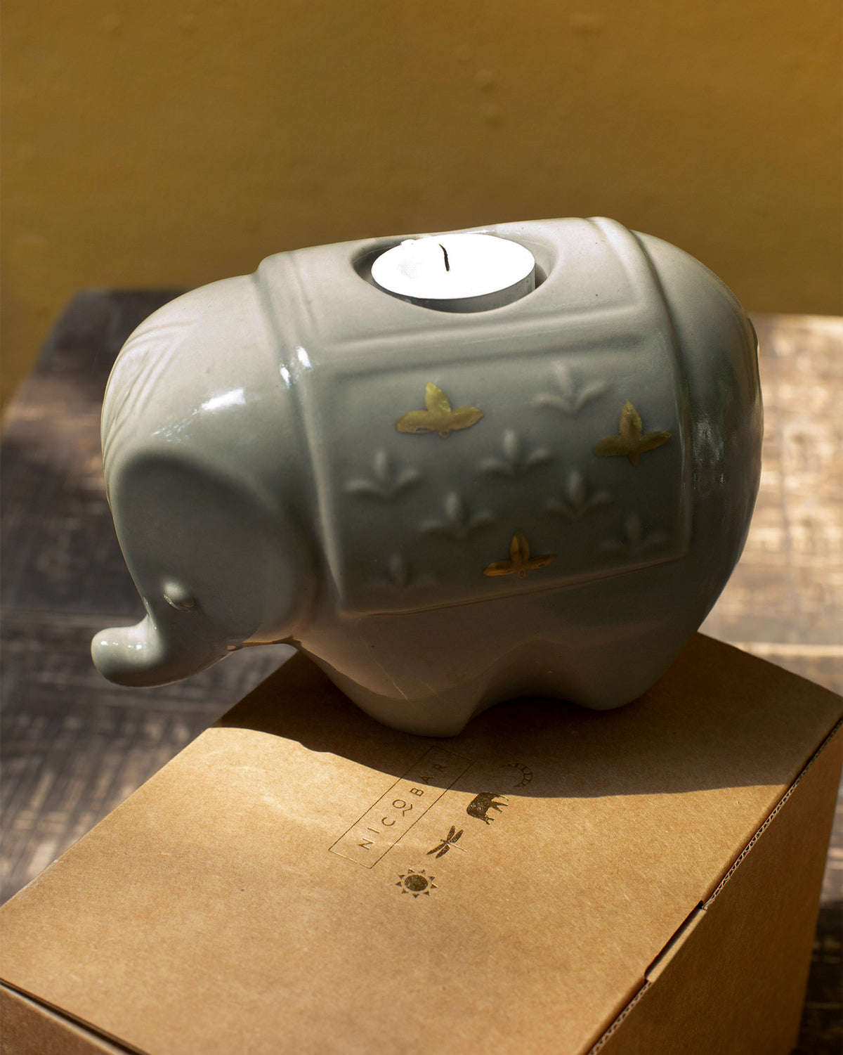 Ele votive in grey-green ceramic with a tealight, set on its kraft box.
