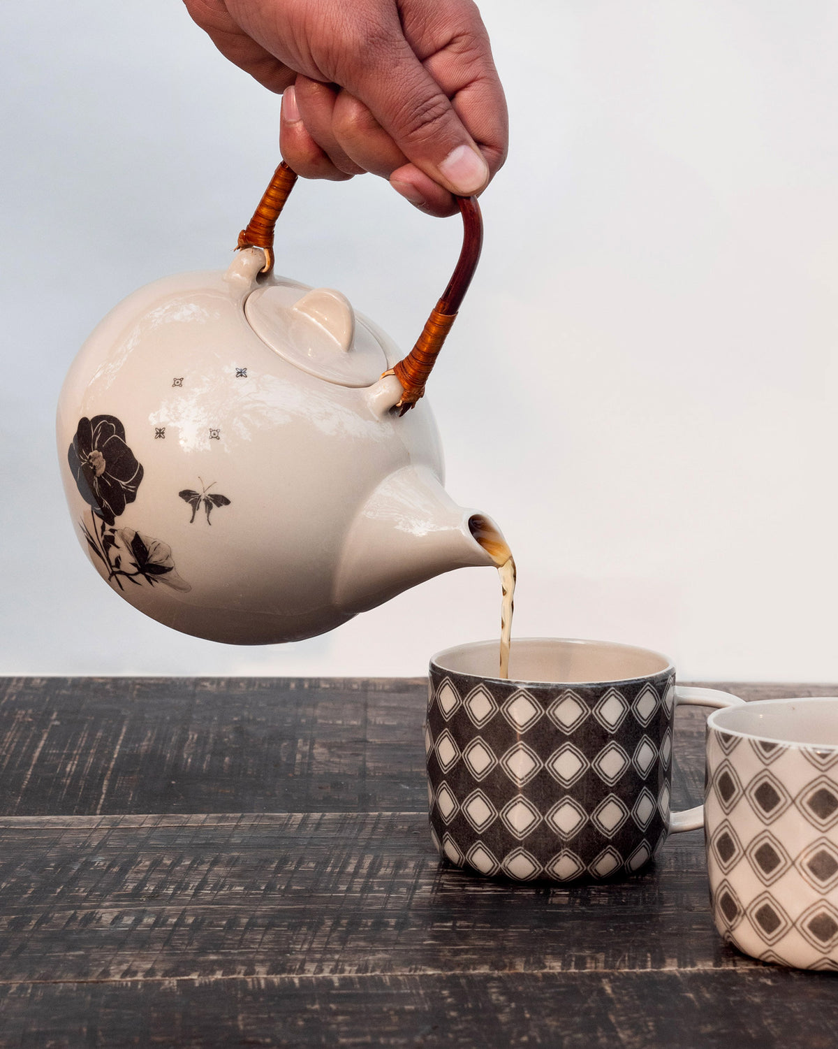Hand pouring tea from a Poppy teapot into a geometric mug.