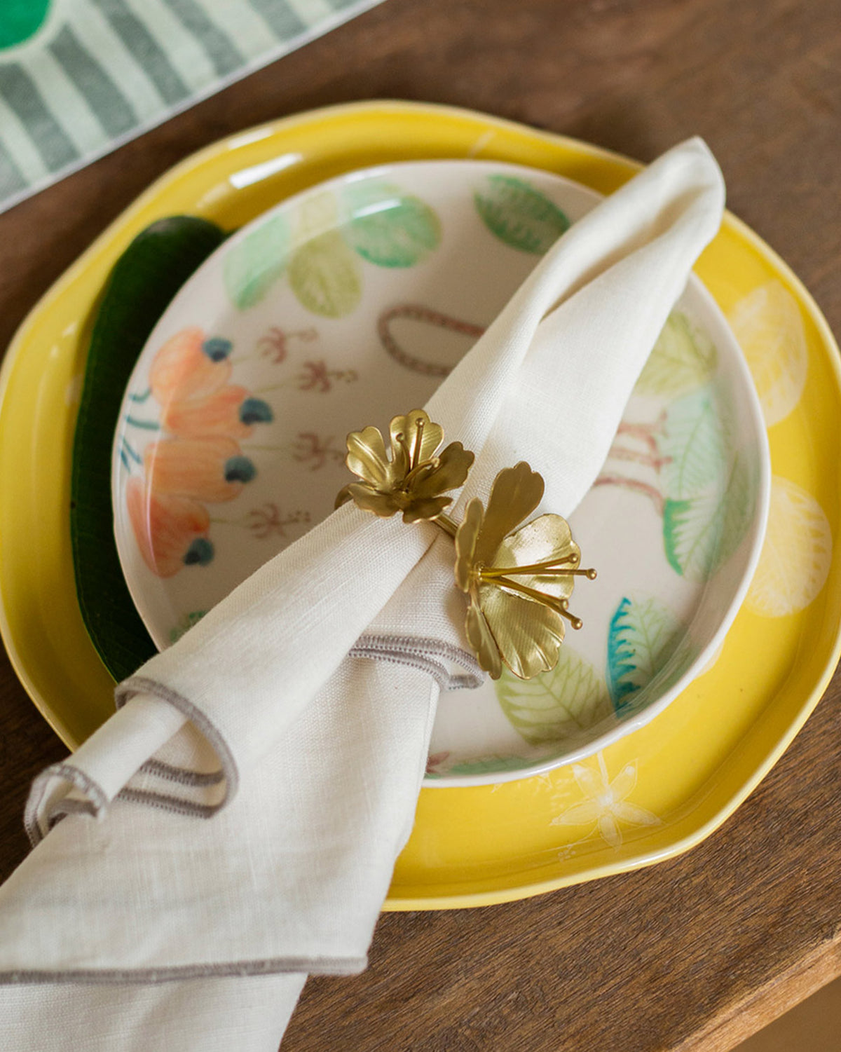 Kachnar Napkin Rings with brass-toned flower motifs holding a folded napkin.