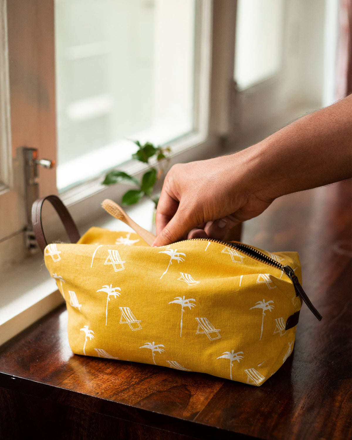 Coast Toilet Case being unzipped by hand, showing its yellow palm tree print.