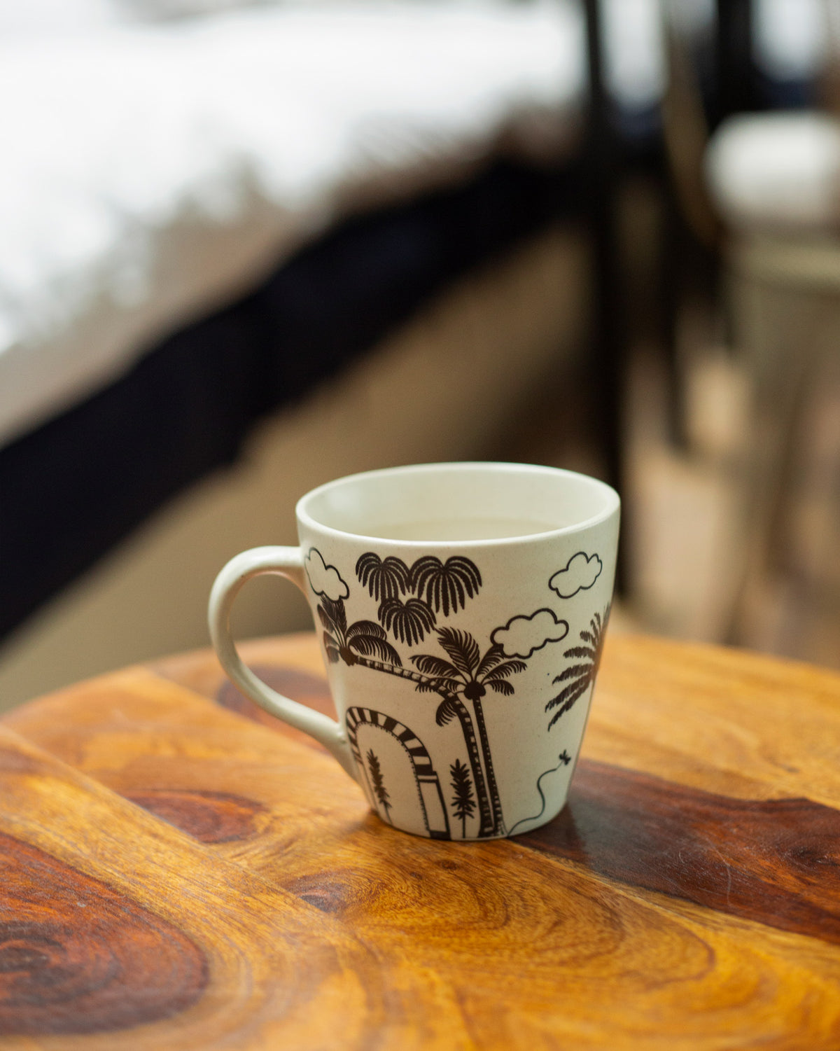 Mandovi Palm Mug with black palm trees and clouds on a wooden table.