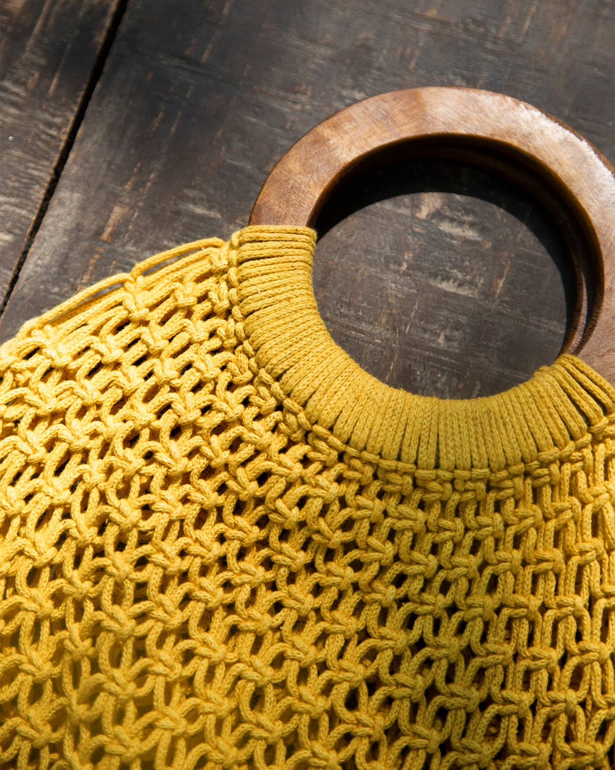 Close-up of a Mandovi Bag showing its yellow mesh weave and wooden ring handle.