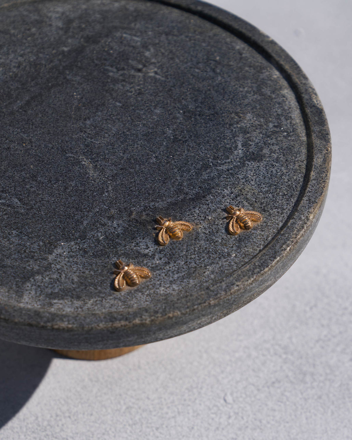 Angled view of a Firefly cake stand showing three gold fireflies on dark marble.