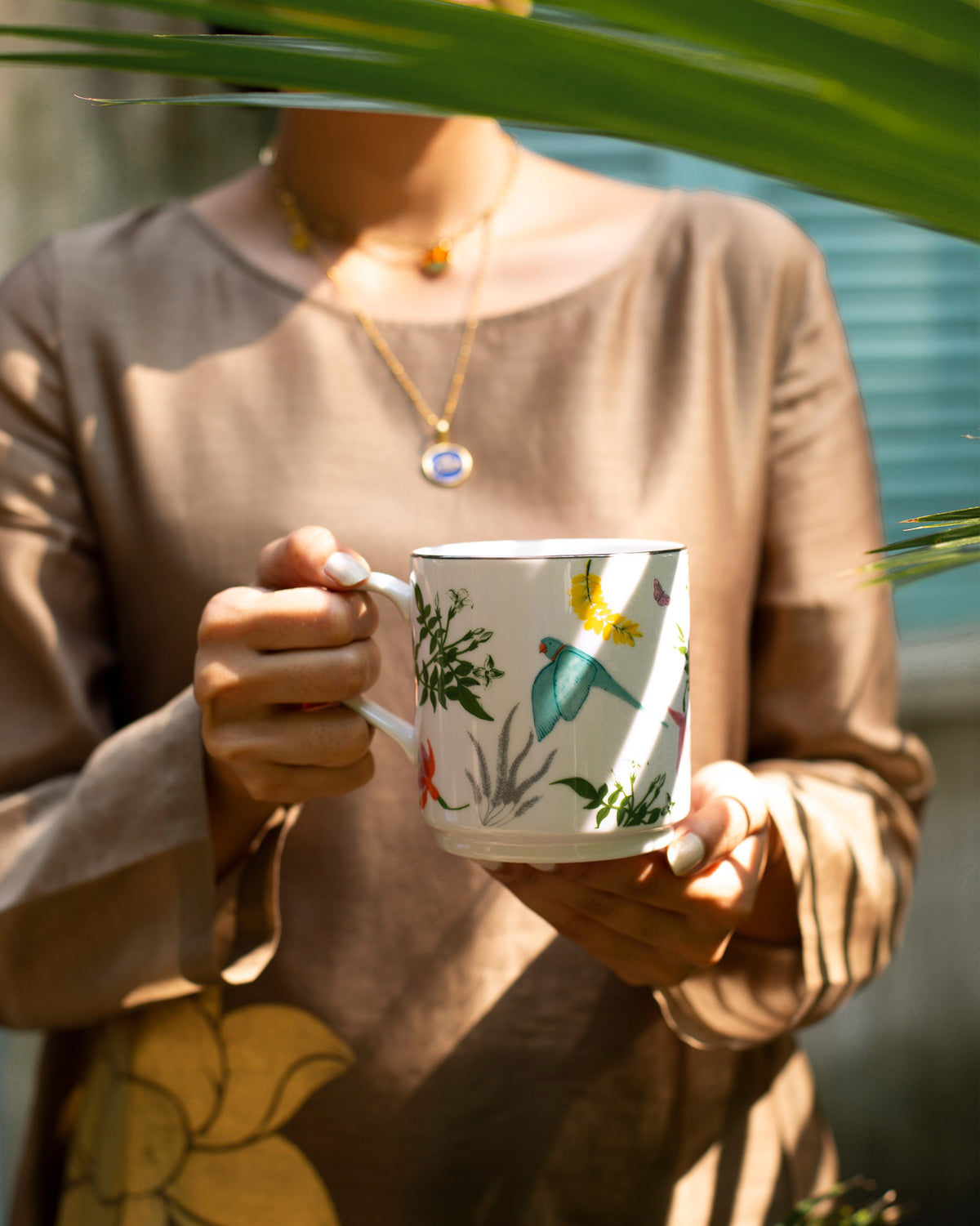 Person holding a Tota Mug with a green bird and botanical print.