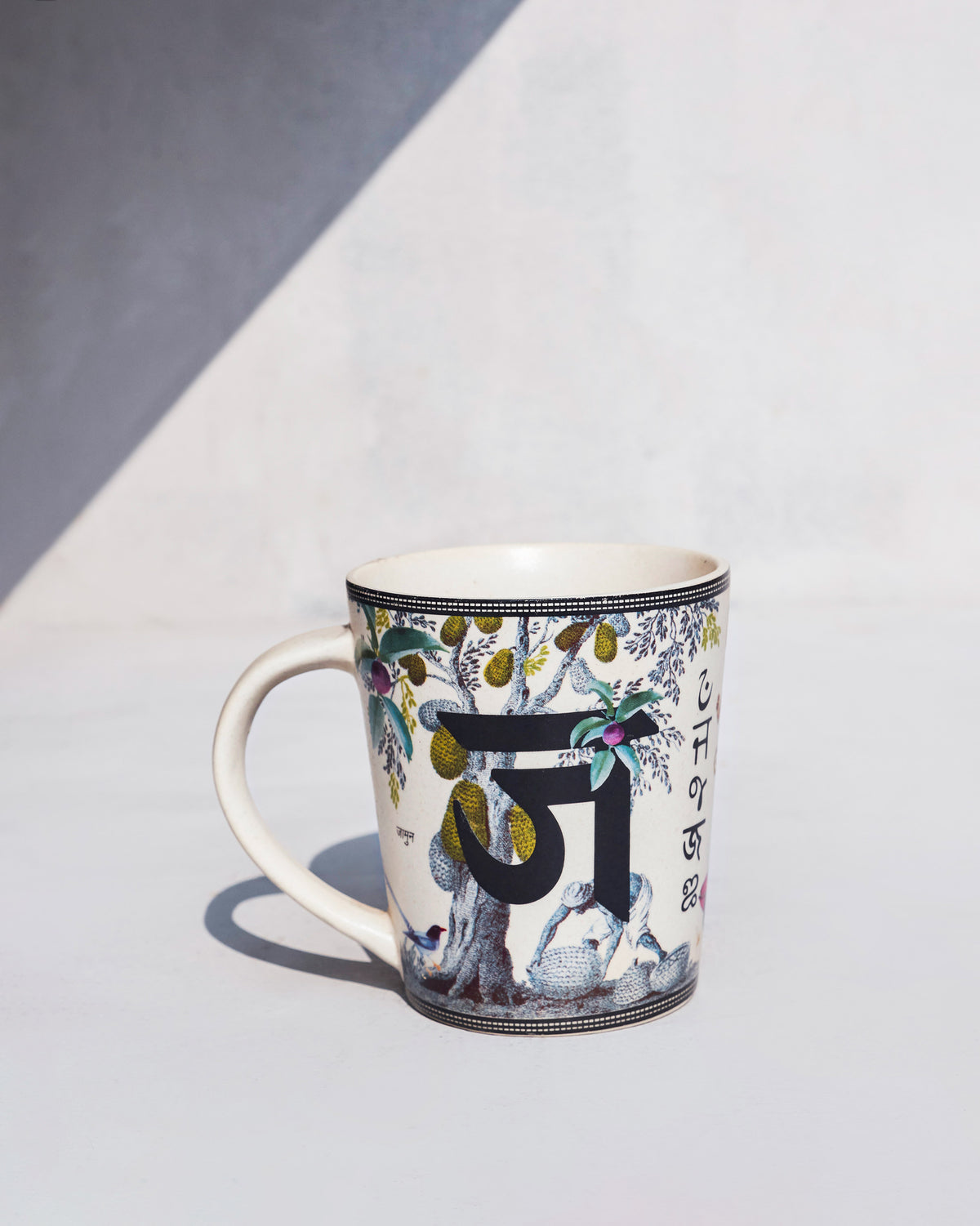 Side view of Jungle mug with a fruiting tree and a small bird printed on it.