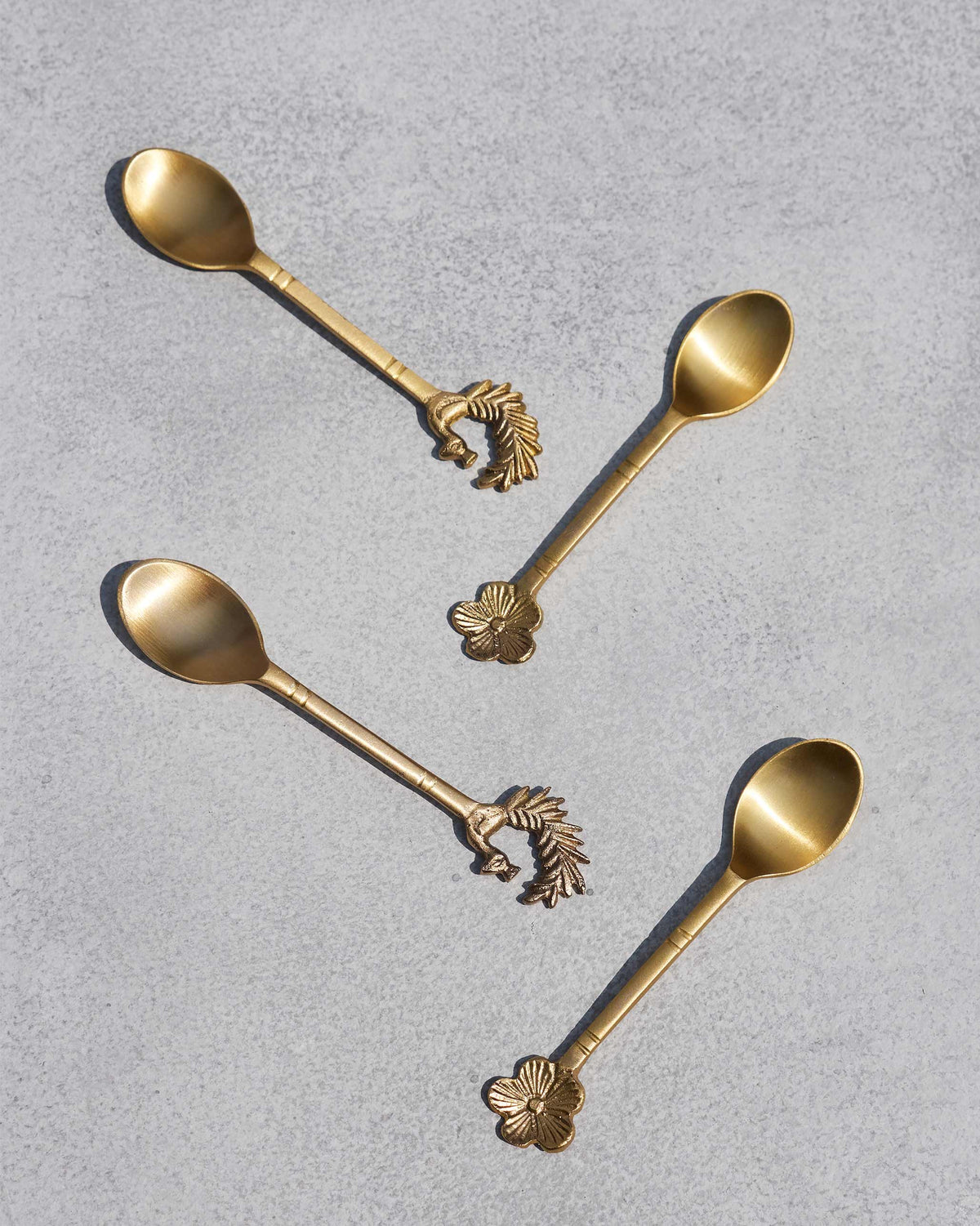 Four brass Mizo coffee spoons laid diagonally with peacock and flower tips.