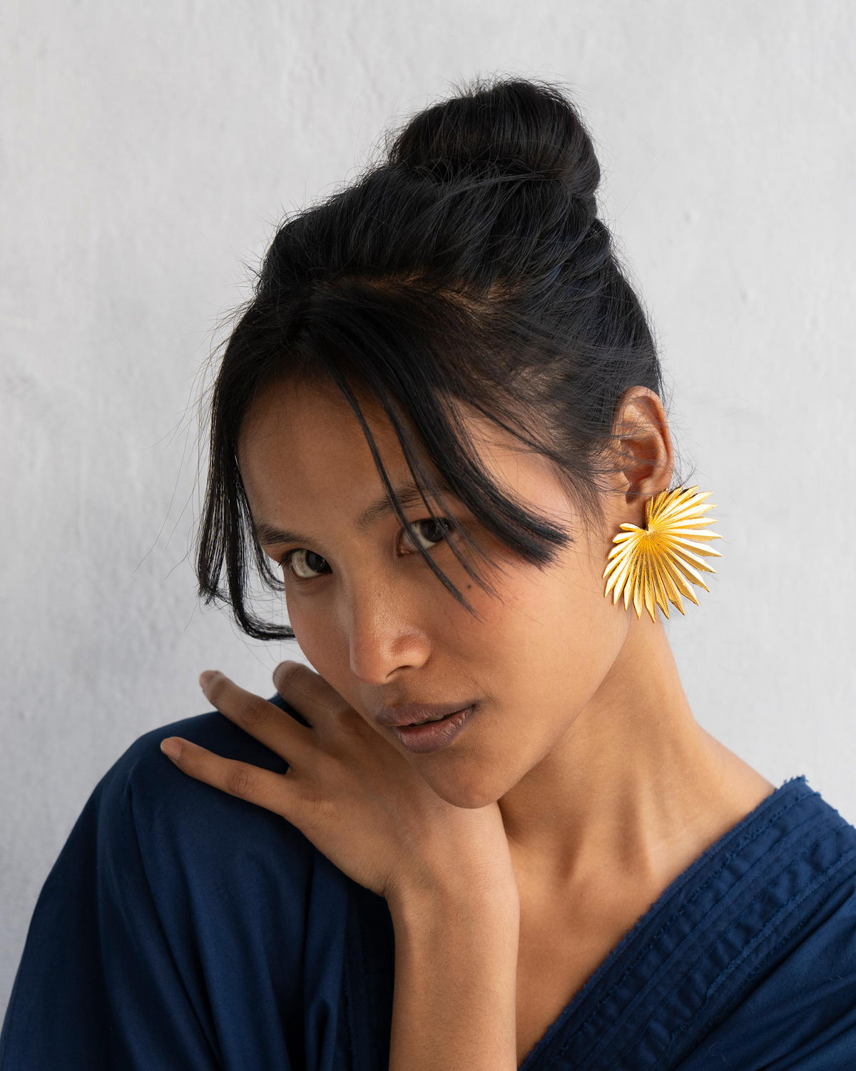 Gold palm leaf earrings worn at a three-quarter angle, showing scale.