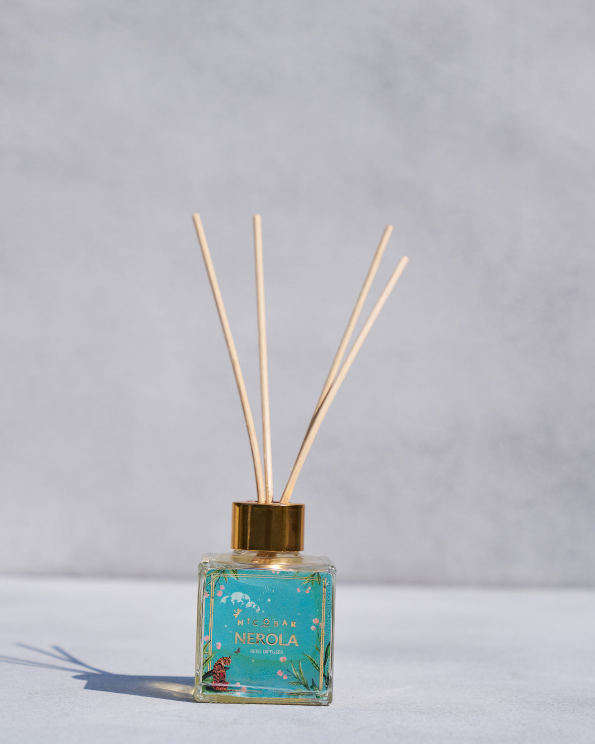 Nerola reed diffuser with a teal glass bottle, gold cap and reeds.