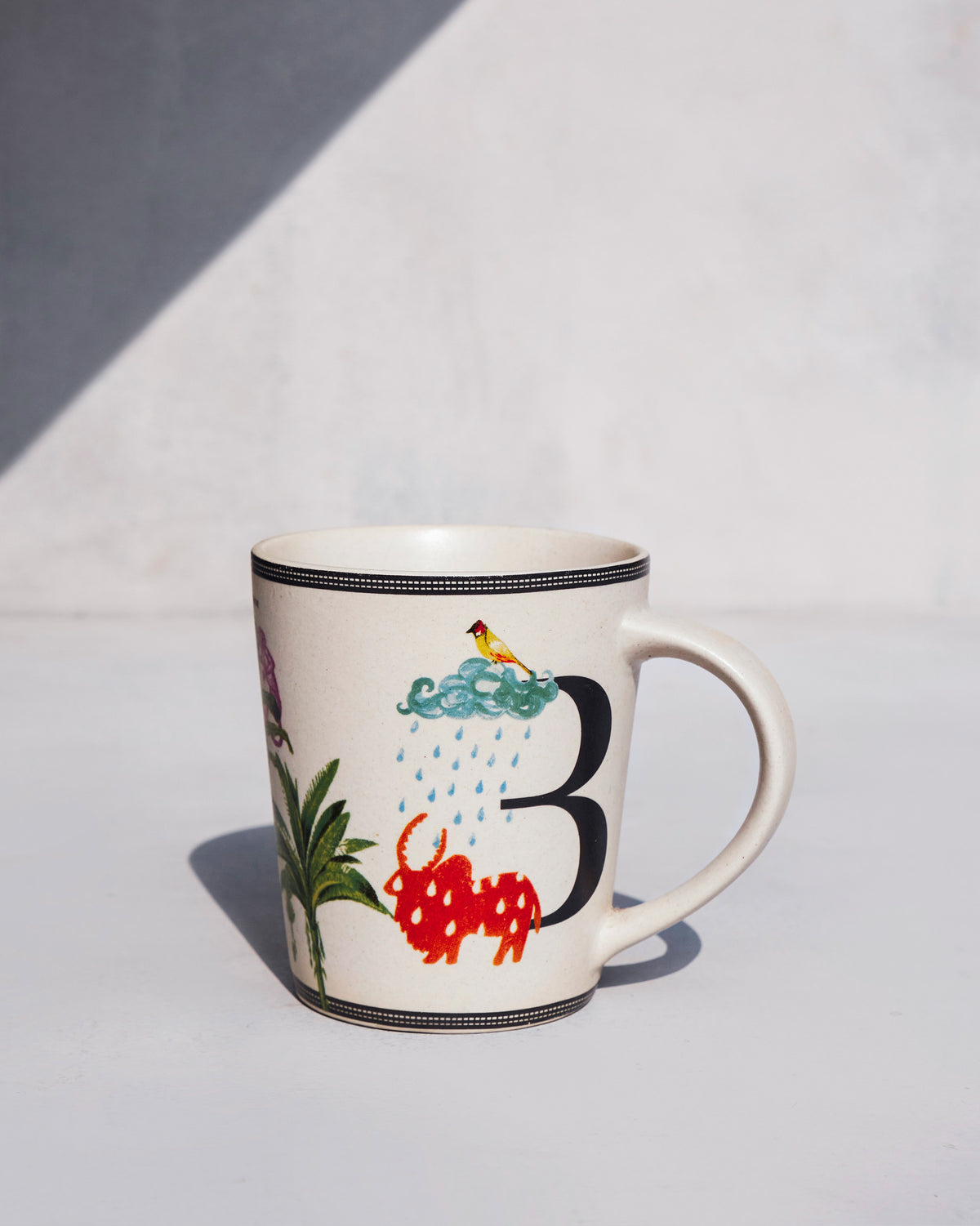 Cream Badal mug with the letter B, bull, and rain-cloud motifs.