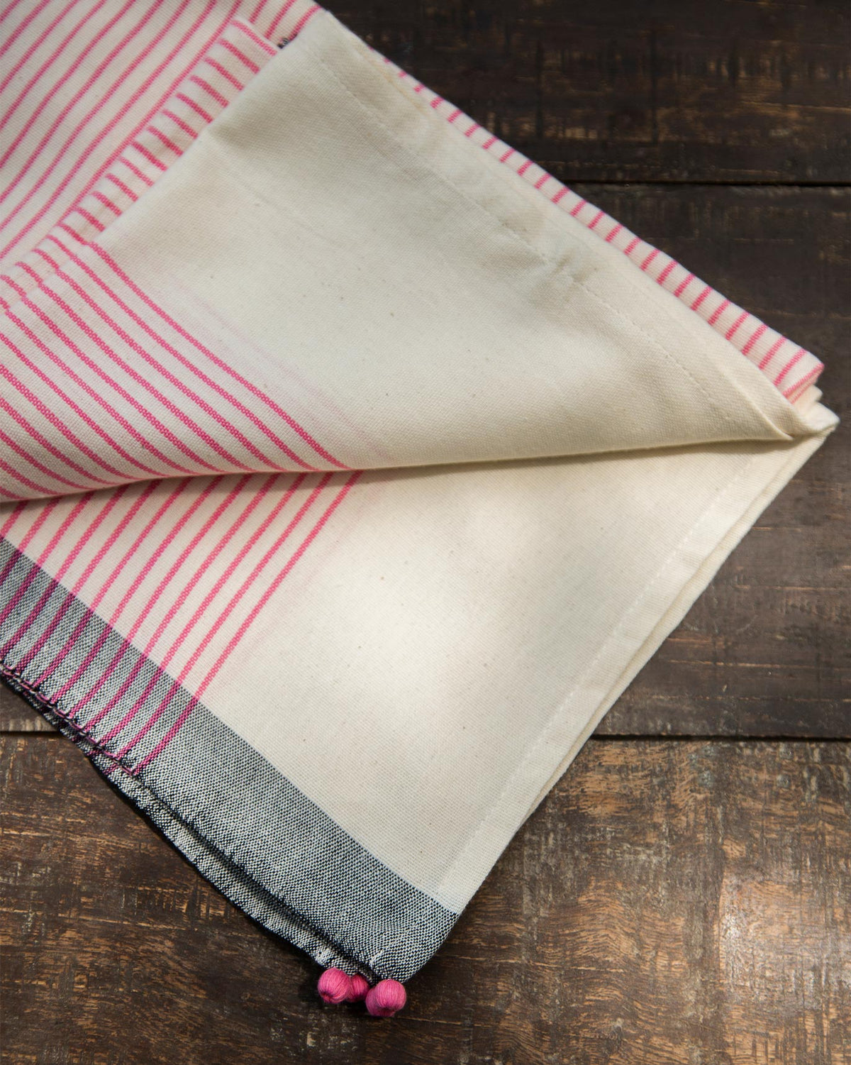 Folded Coast Towel in pink stripes with pom-pom ends.