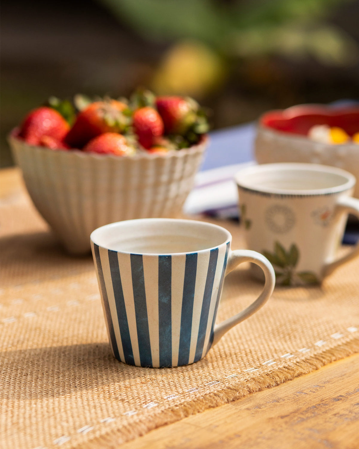 Striped Nadi Espresso Mug on a jute mat, beside a floral mug.