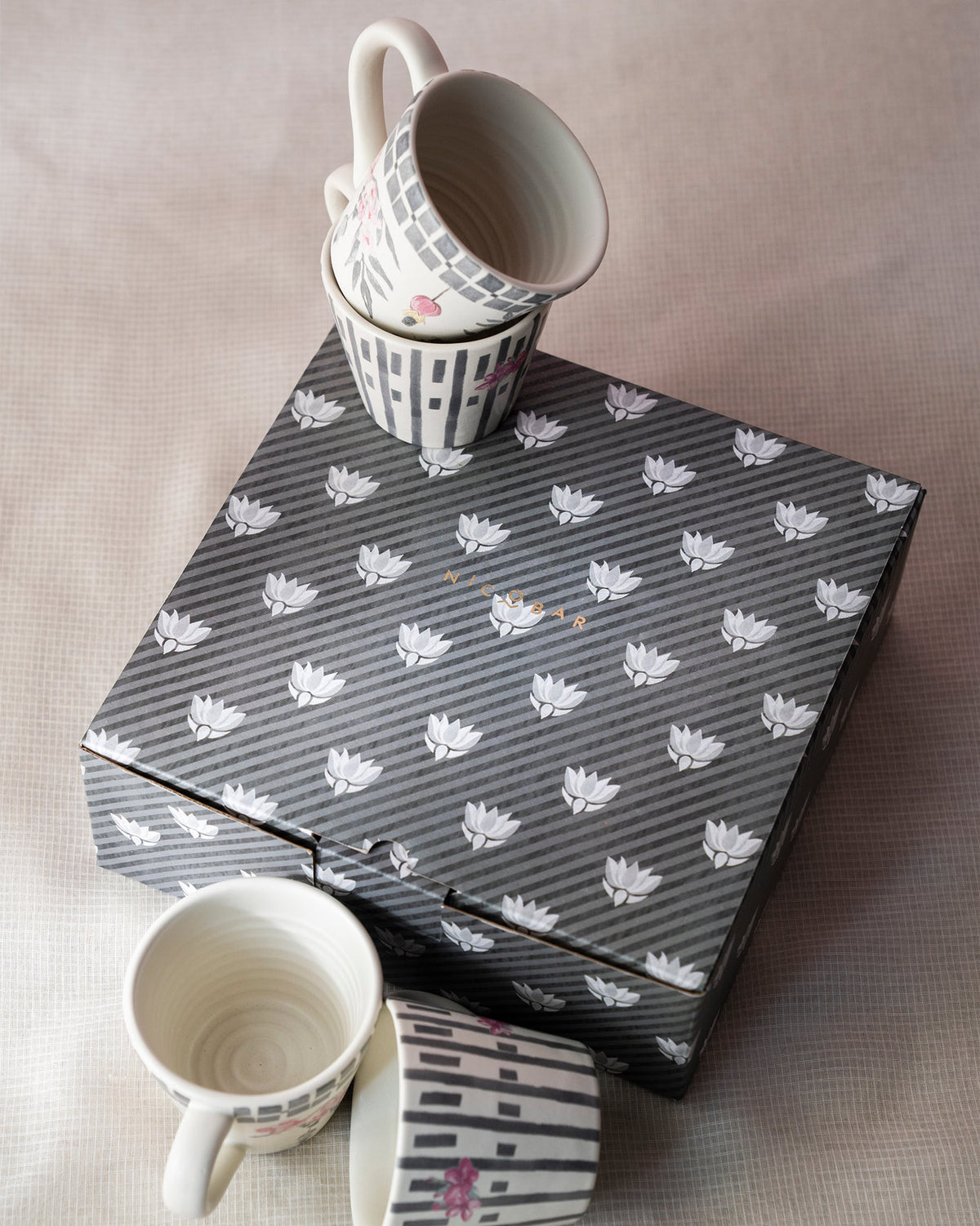 Set of four Nectar espresso mugs with pink florals beside a striped lotus gift box.