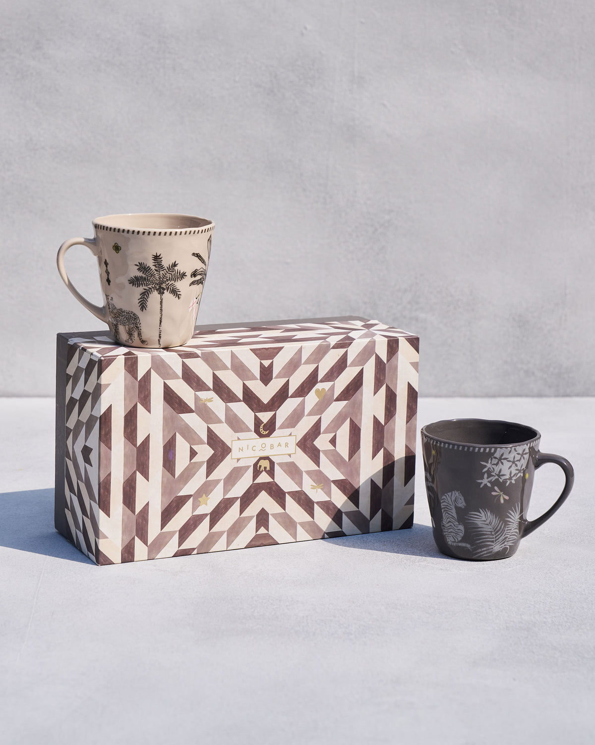 Malabar conical mugs with tiger and palm motifs beside a geometric gift box.