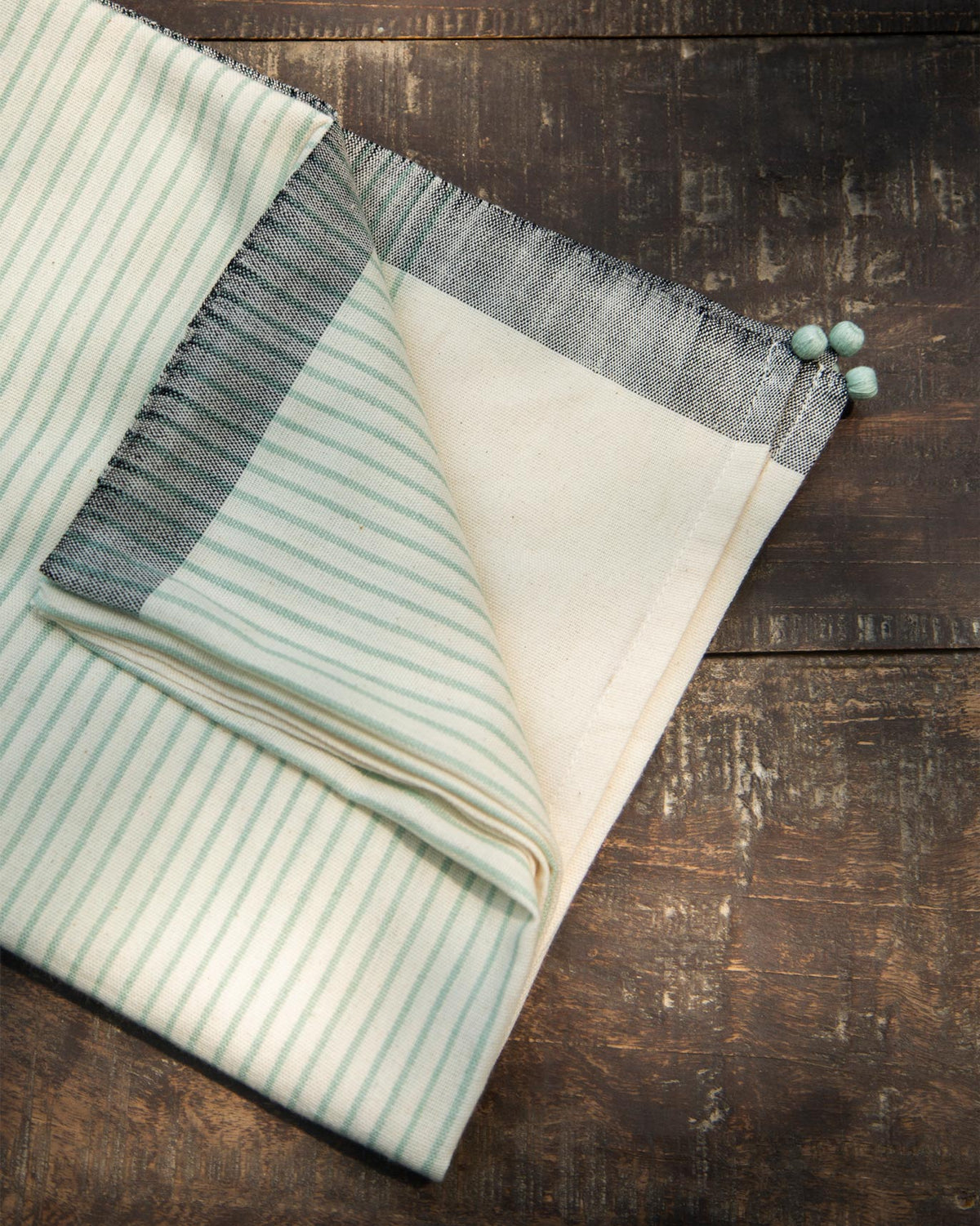 Folded Coast Towel in aqua stripes with pom-pom ends.
