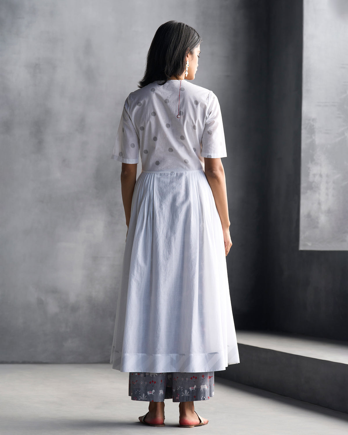 Back of a white front-overlap yoke kurta with grey dots and flared hem.