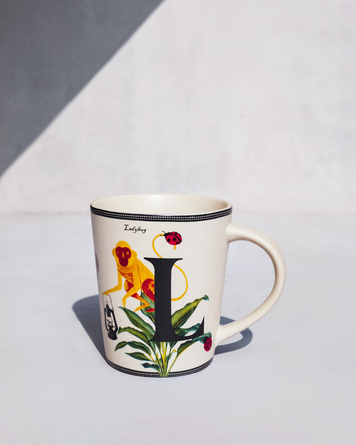 Cream Langoor mug with letter L and a yellow monkey holding a lantern.