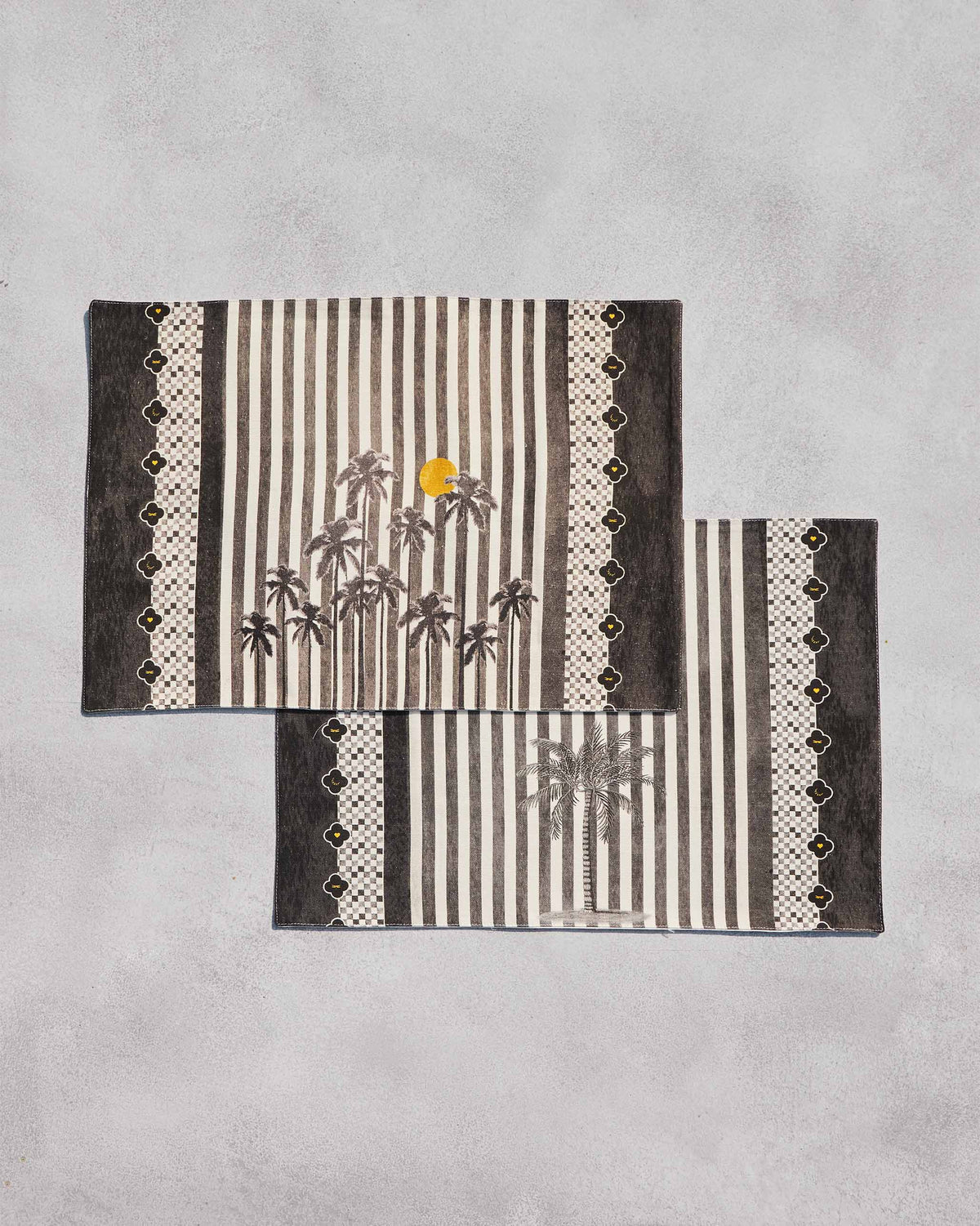 Angled view of a pair of Midnight placemats with palm trees.