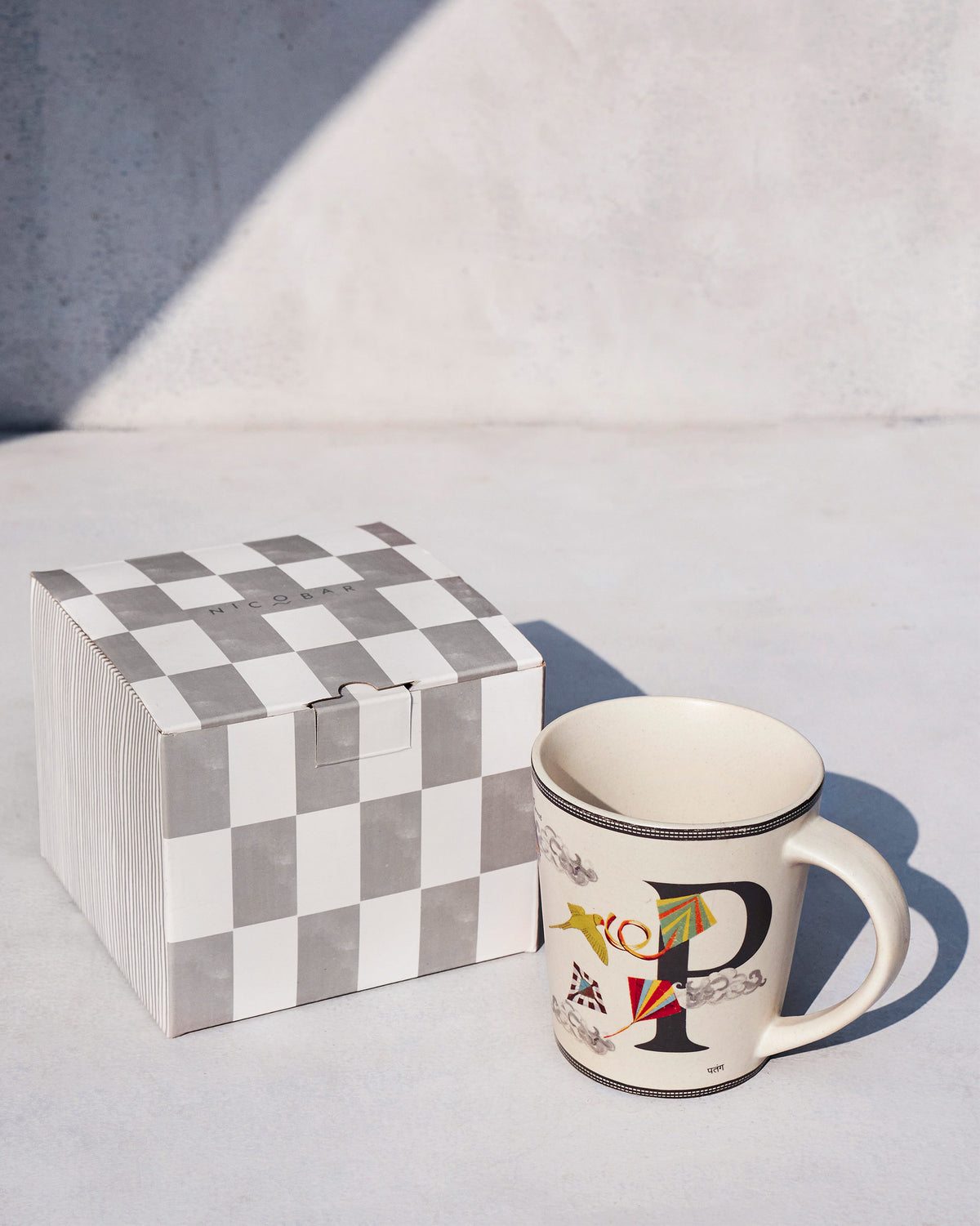 Patang mug with kite motifs standing beside its checkered Nicobar box.
