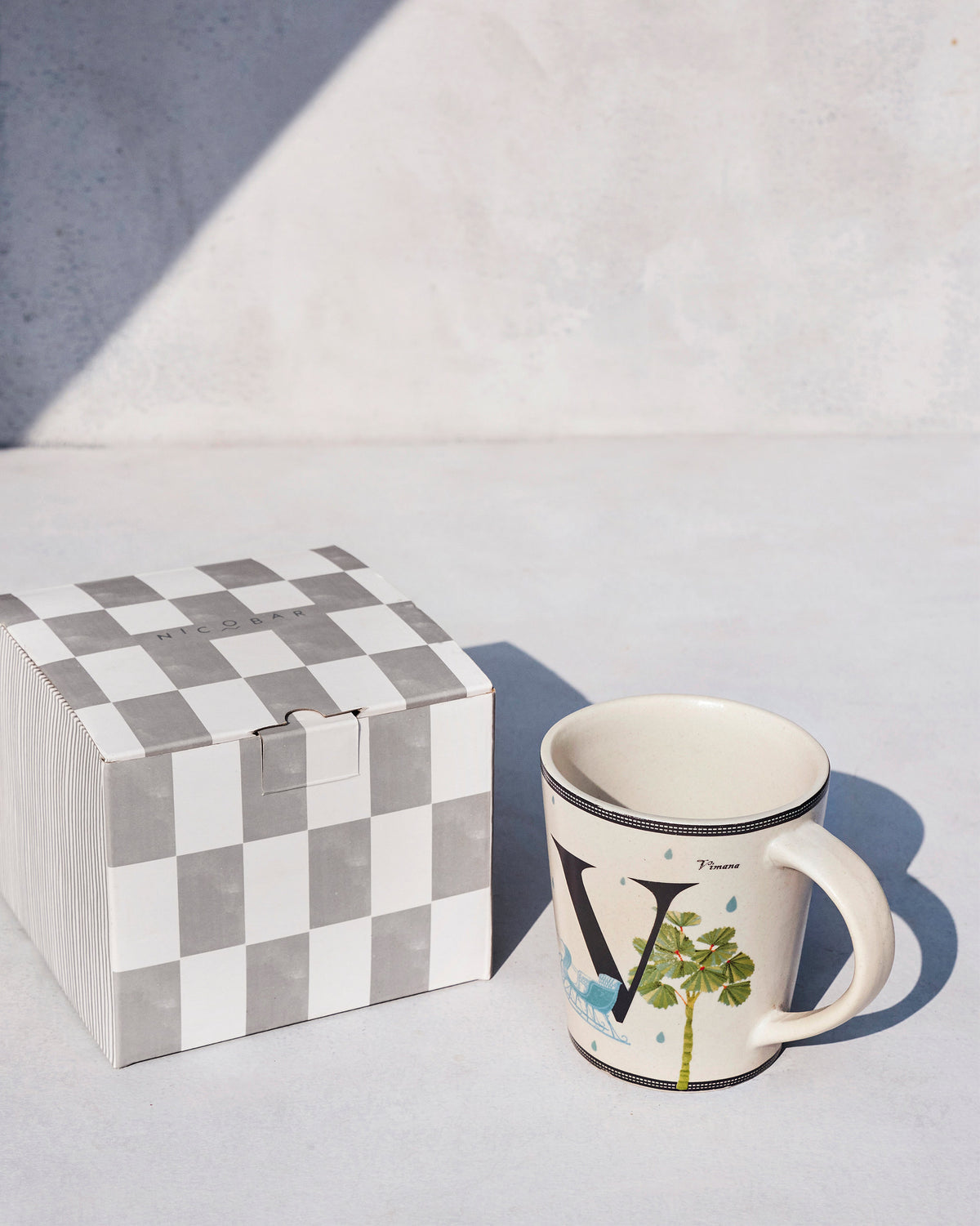 Vriksh mug standing beside its grey check Nicobar gift box.