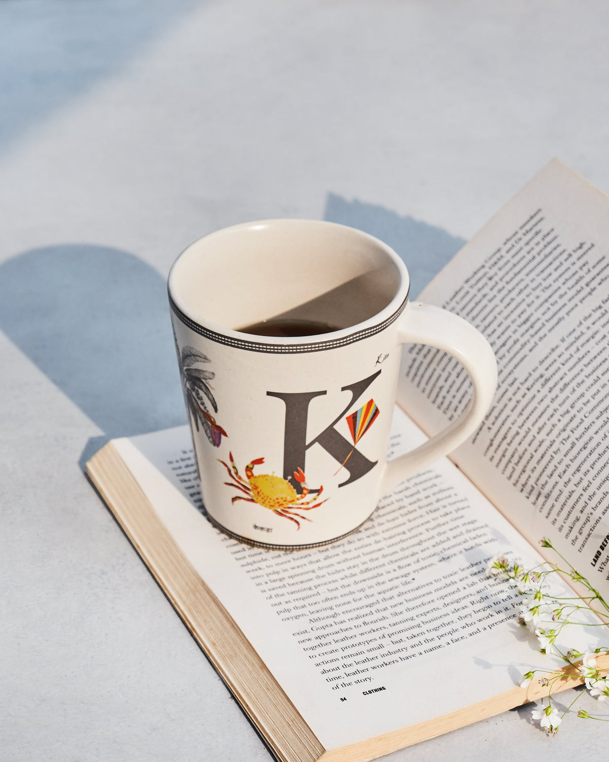 Cream Kamal mug with letter K motifs resting on an open book.