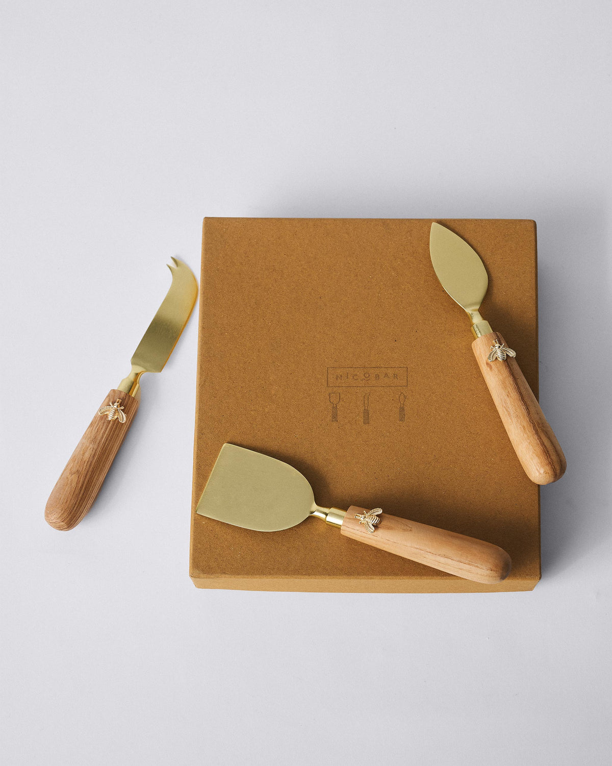 Garo cheese knives with bee charms arranged around a kraft Nicobar gift box.