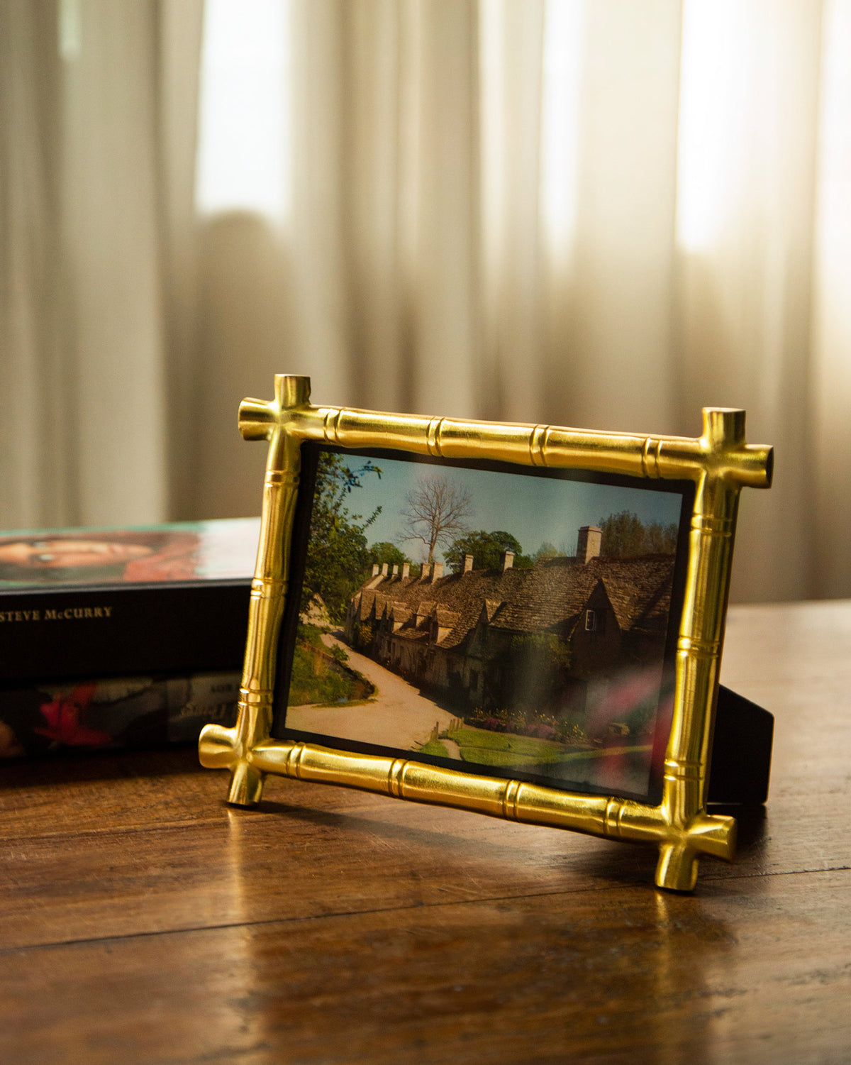 Gold bamboo photo frame holding a landscape photo on a table.