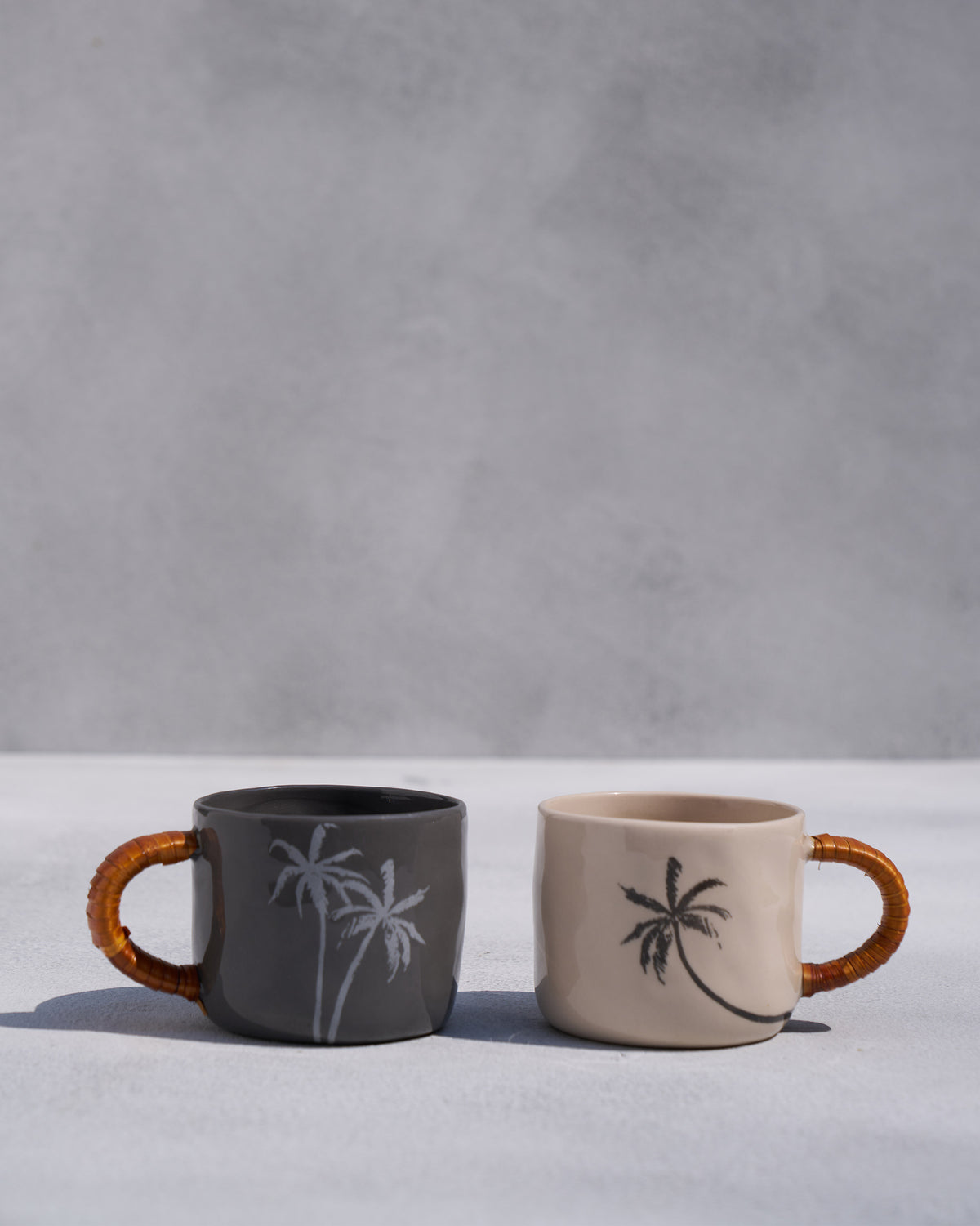 Charcoal and ivory Mandovi mugs with palm motifs and woven handles.