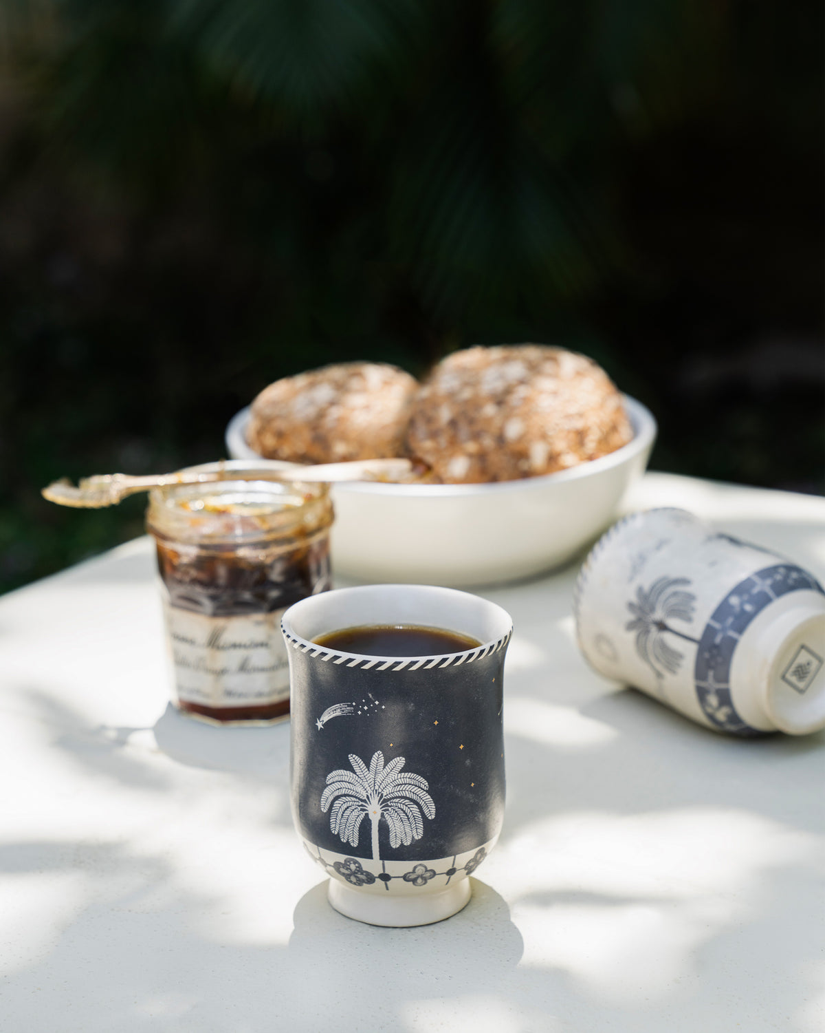 Navy Twilight Tea Cup with a palm tree motif, filled with a dark drink.