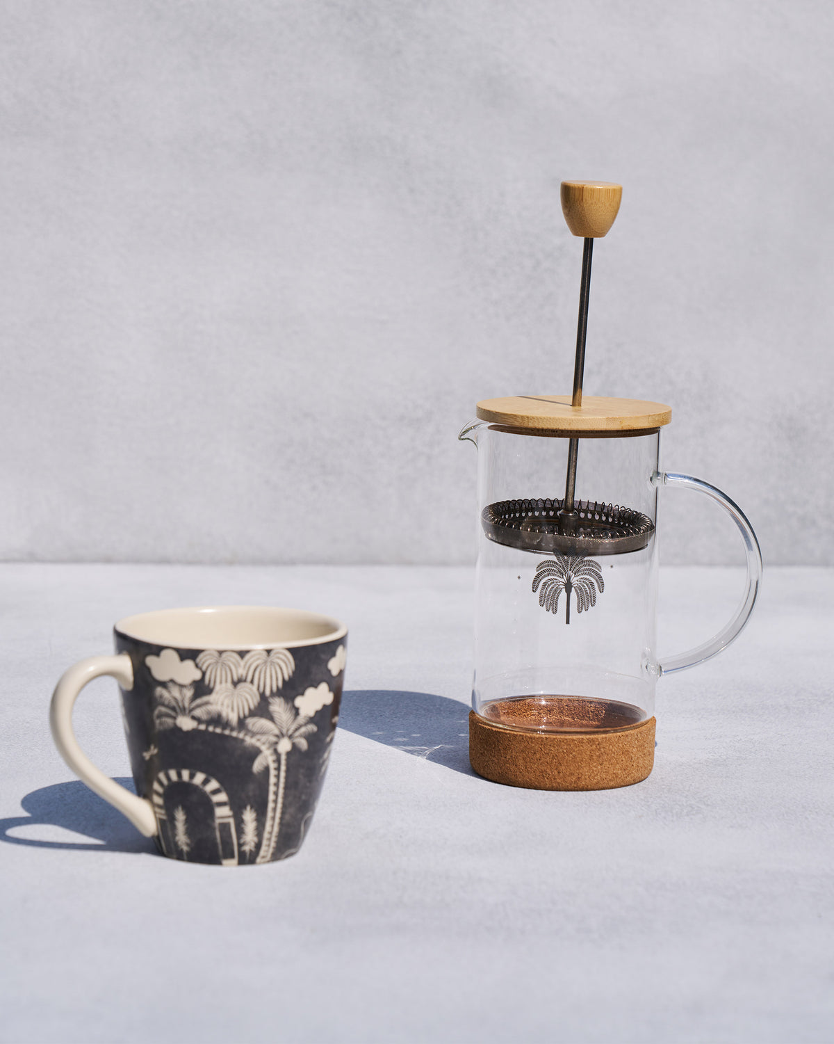 Toddy French press with wooden lid beside a charcoal palm-print mug.
