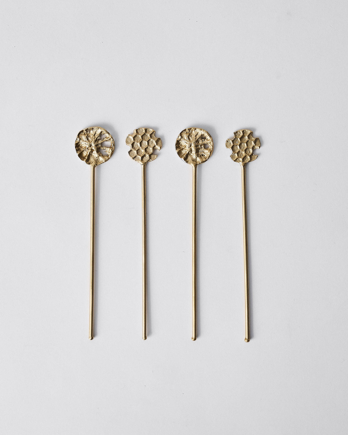Four gold Dawa stirrers with floral and honeycomb tops laid in a row.