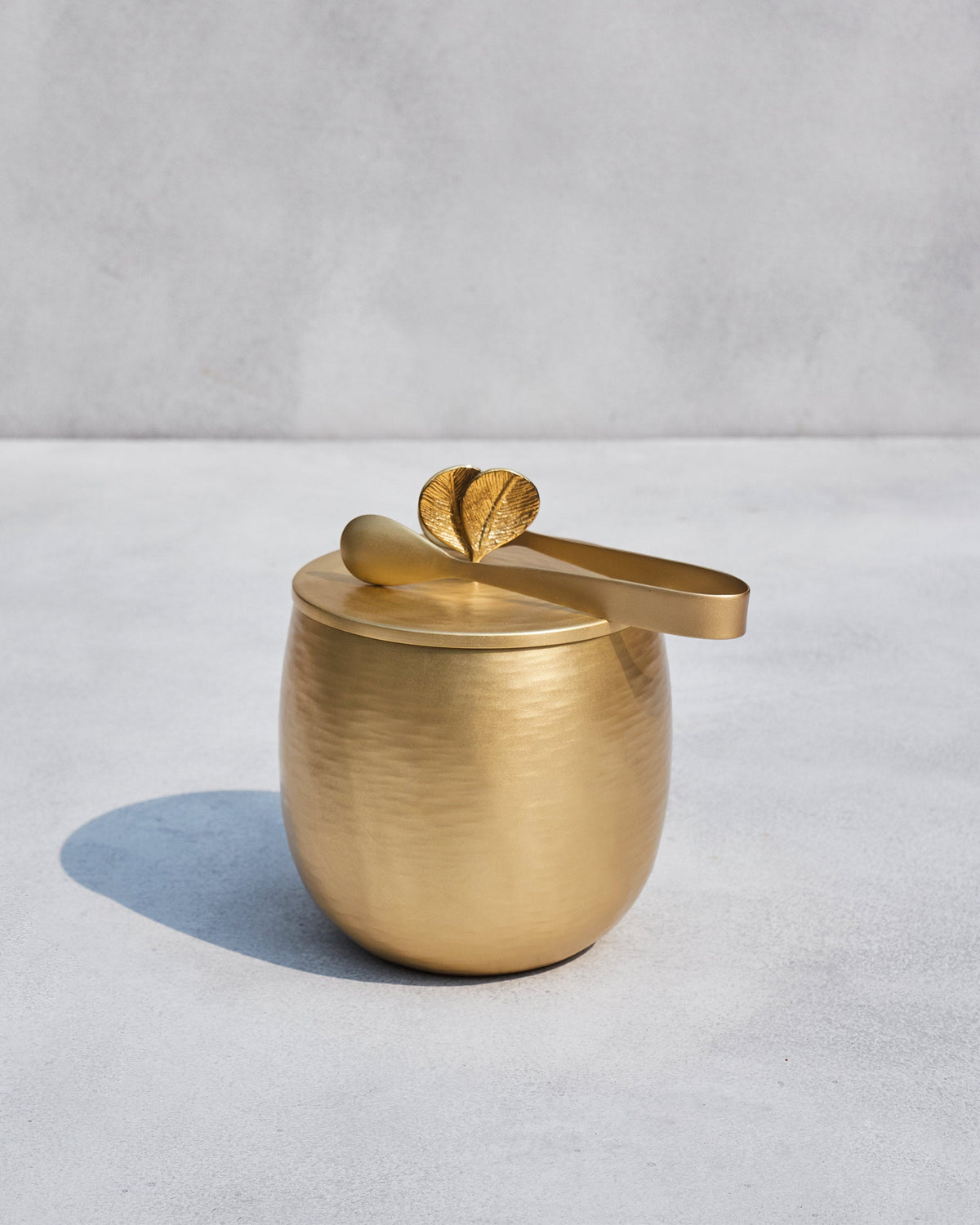 Gold Champa ice bucket with tongs resting on the leaf-topped lid.