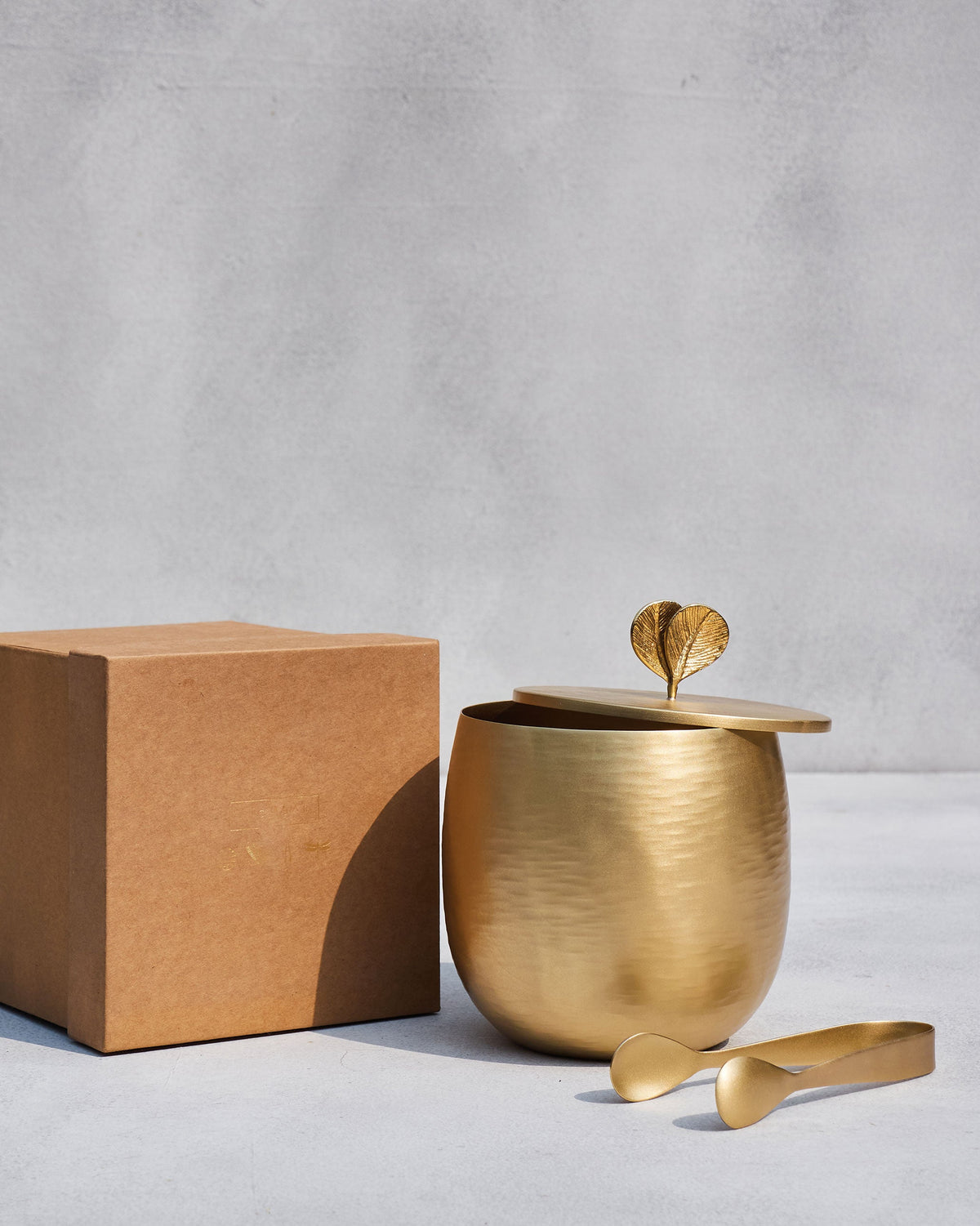 Gold Champa ice bucket and tongs beside a brown gift box.