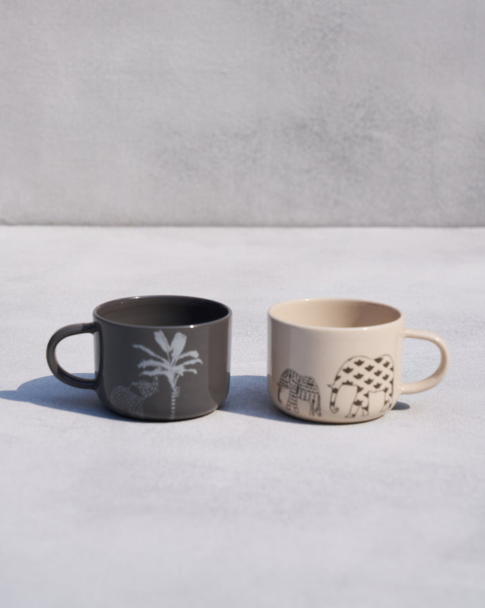 Pair of Coastal Mugs in charcoal and cream with palm and elephant motifs.