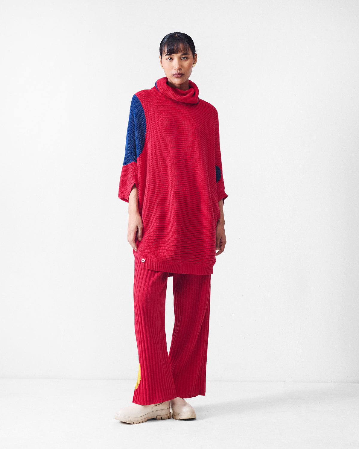 Person wearing red rib-knit wide-leg pants with a yellow heart near the hem.