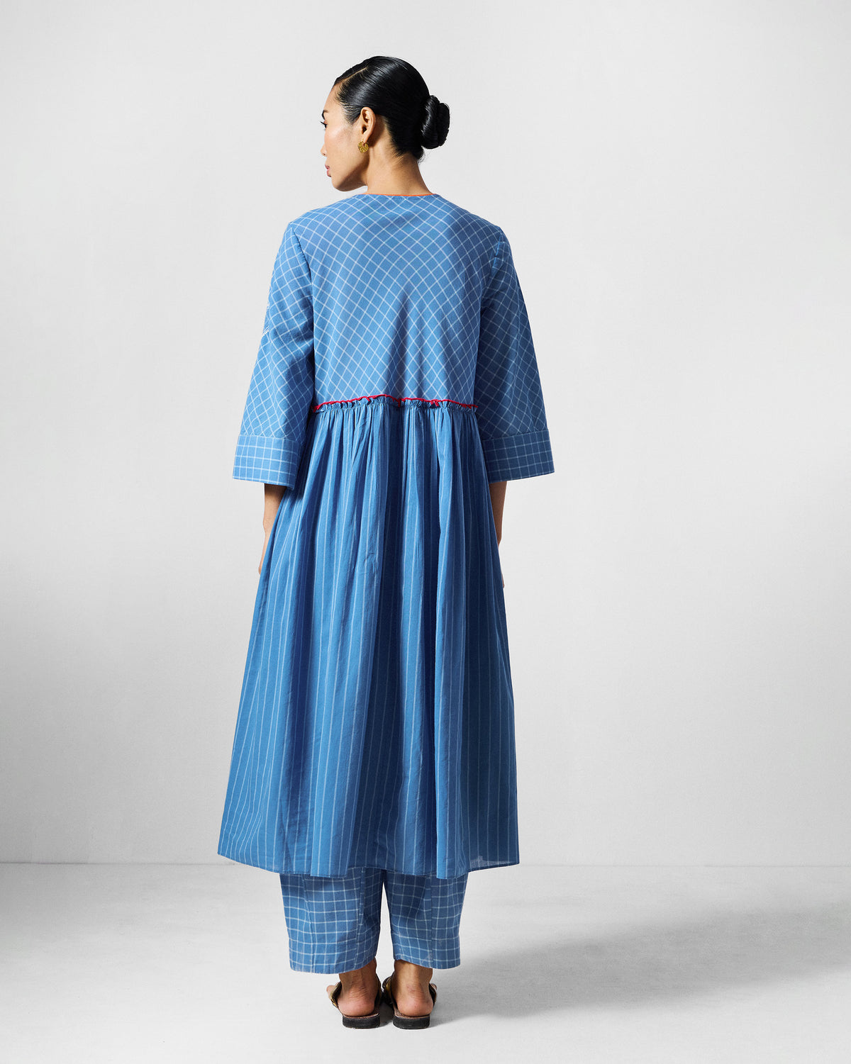 Back of the blue check Giri kurta worn by a person, with gathered waist and red piping.