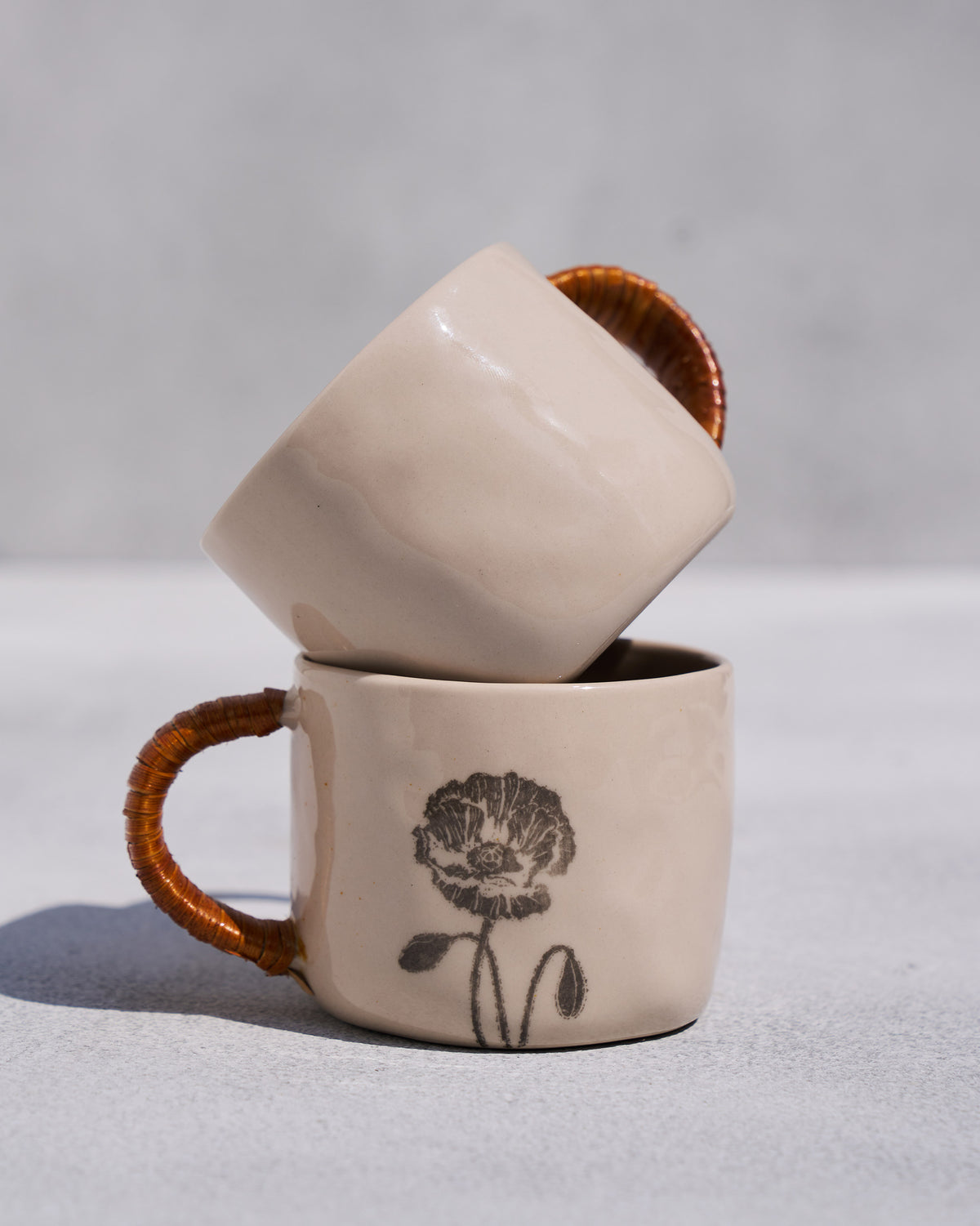 Stacked Poppy mugs with rattan handles and a black poppy print.