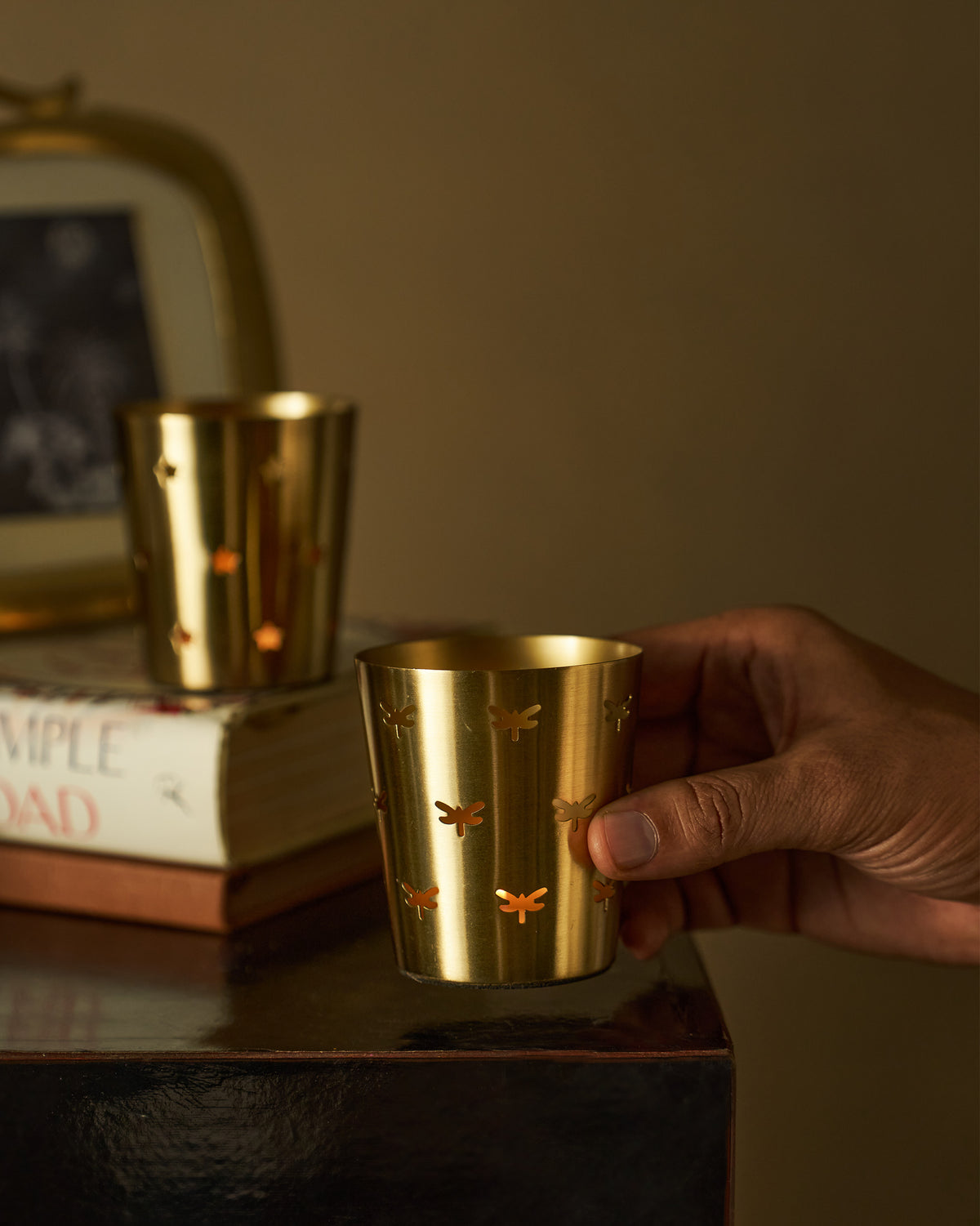 Close-up of a Smriti gold votive with dragonfly cutouts held in hand.
