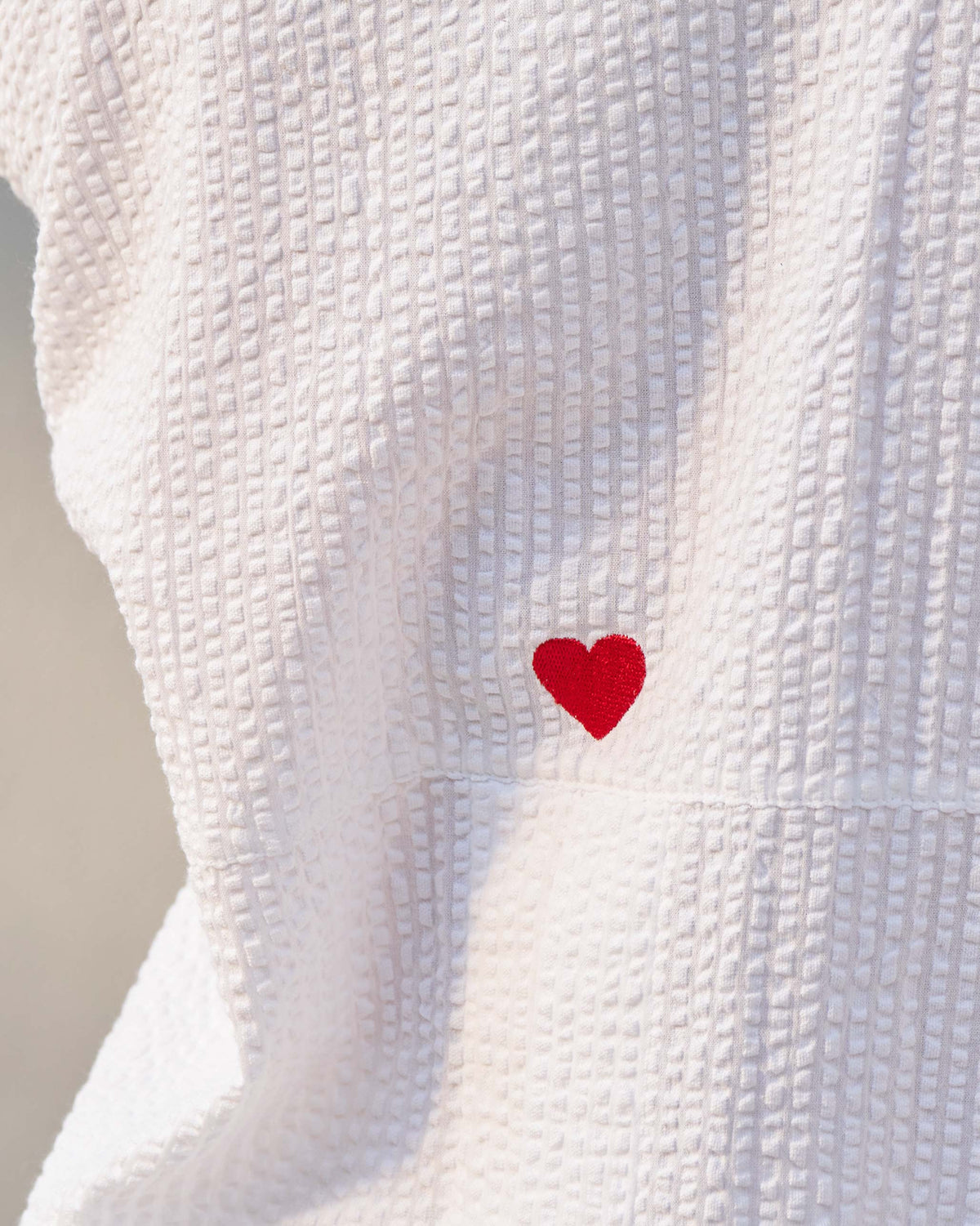 Close-up of a red embroidered heart on white seersucker fabric.