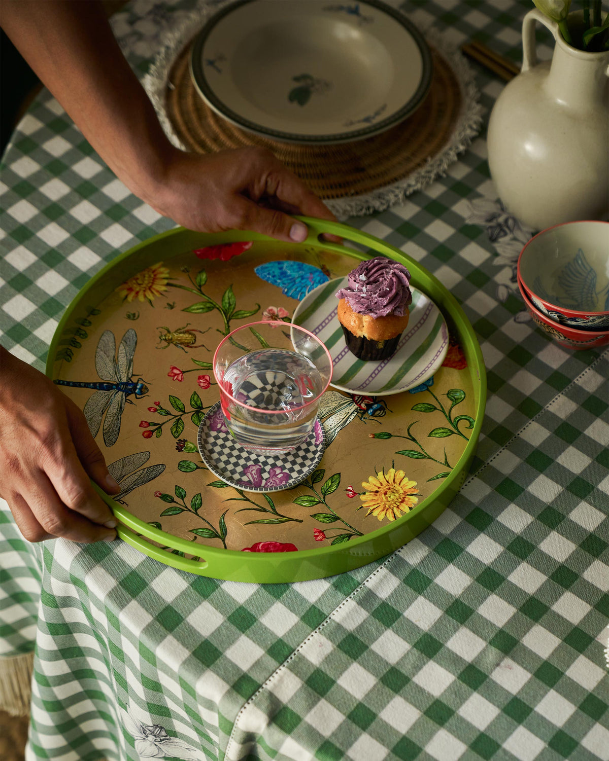 Hands holding a Bloom round tray with a cupcake and glass of water.