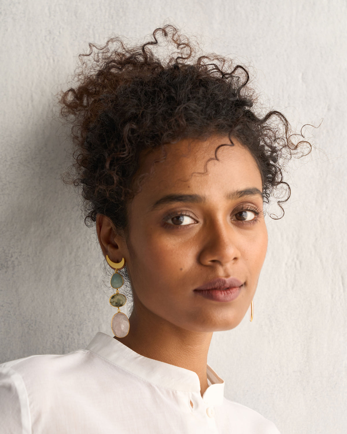 Person wearing Rosy Moon Earrings with a gold crescent and long drops.