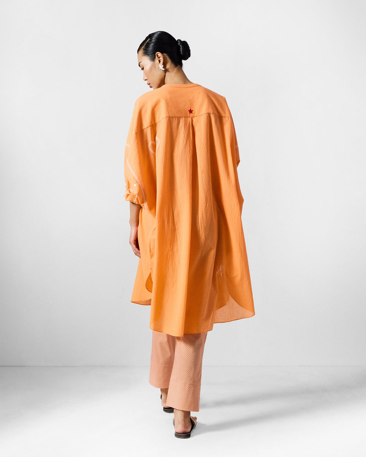 Back of an orange Lazy Sunday tunic with a red embroidered star and box pleat.