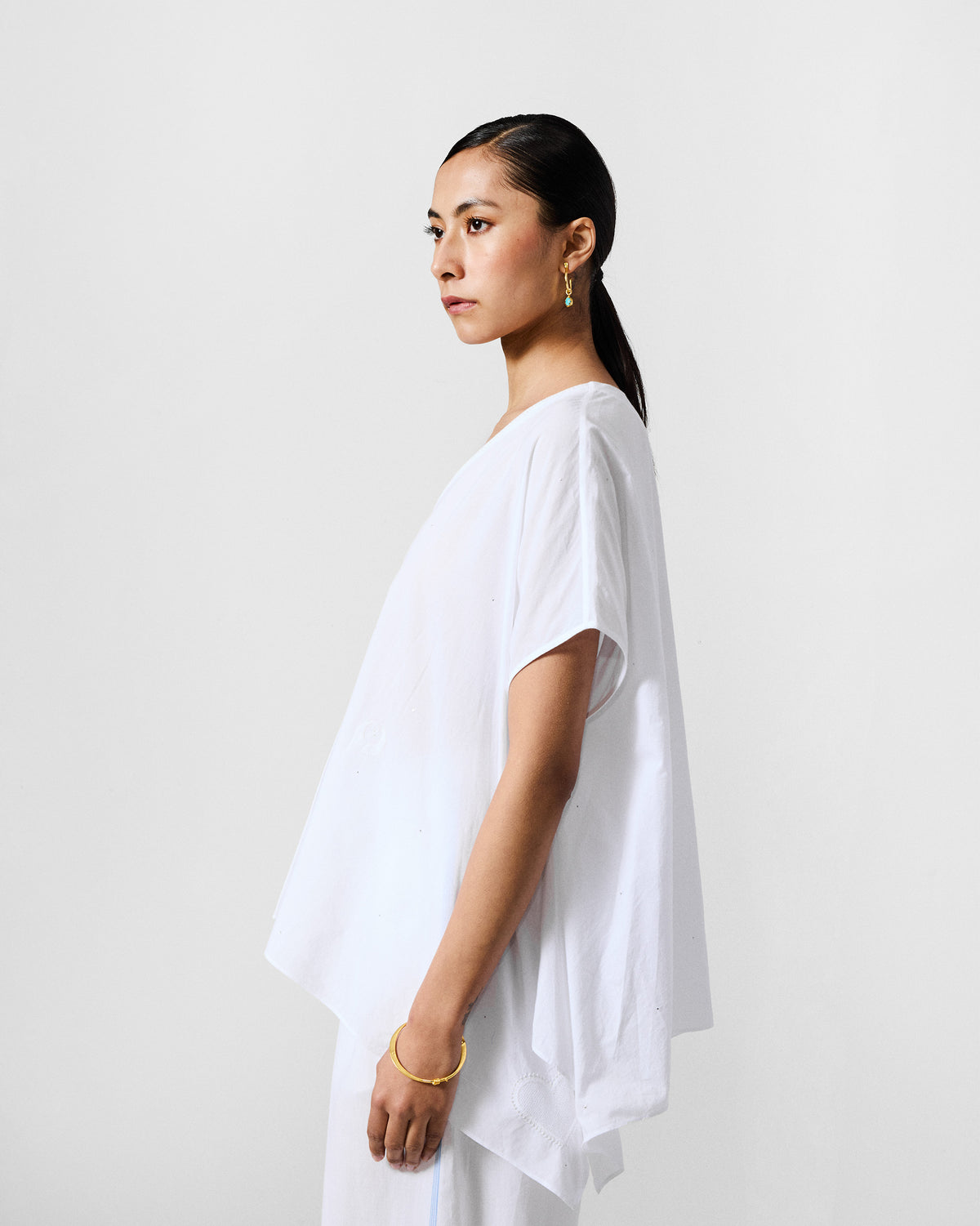 Side view of an ivory Riva top with a draped asymmetric hem.
