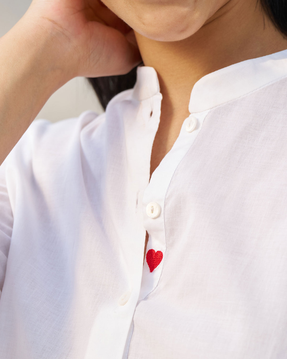 Close-up of a red heart on the placket of a white mandarin collar top.