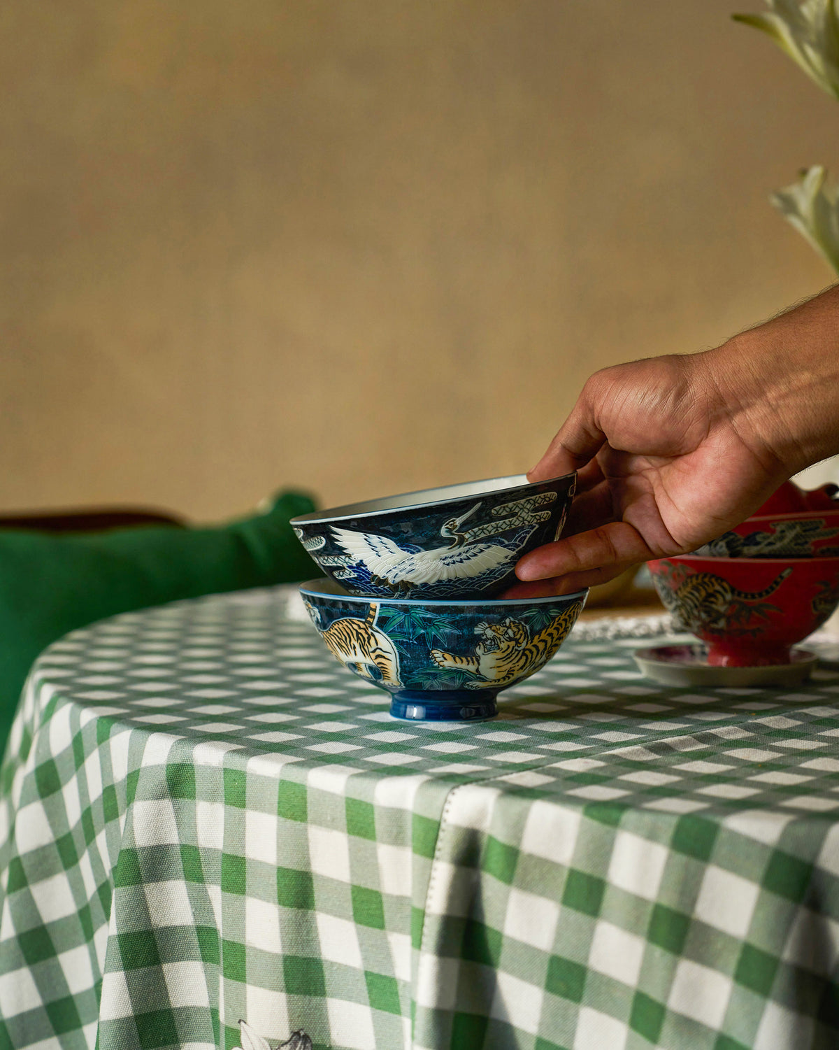 Hand stacking a blue Crane and Tiger Bowl with a white crane motif.